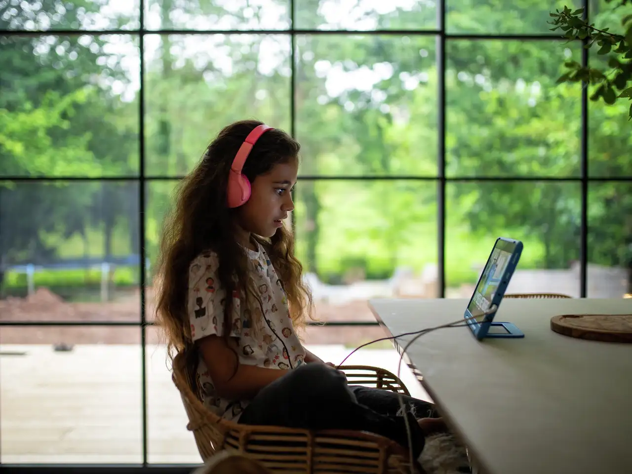 Una bambina siede davanti al suo tablet con le cuffie mentre fuori splende il sole | Rivista VELUX