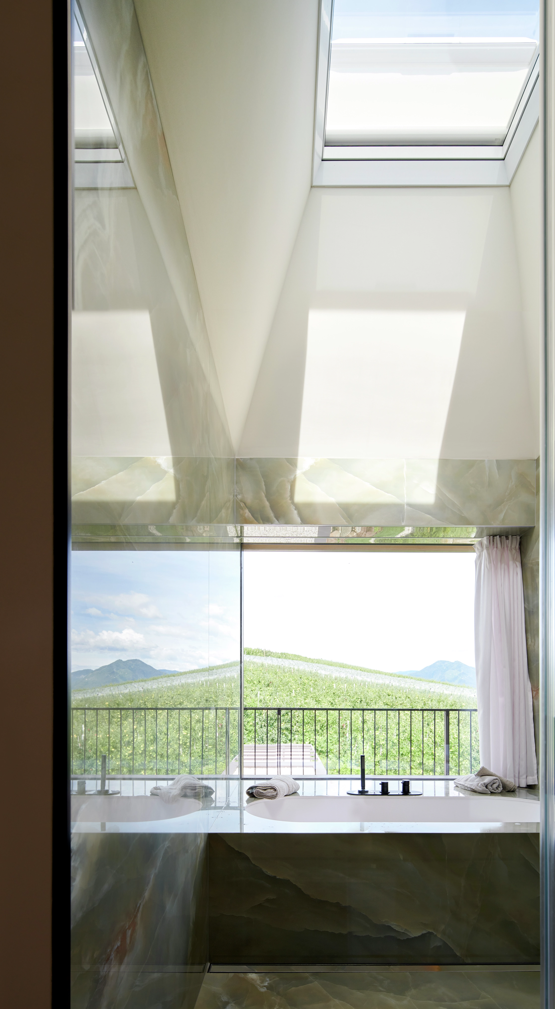 Camera da letto moderna con finestra per tetti VELUX che si affaccia su un paesaggio verde e montagne.