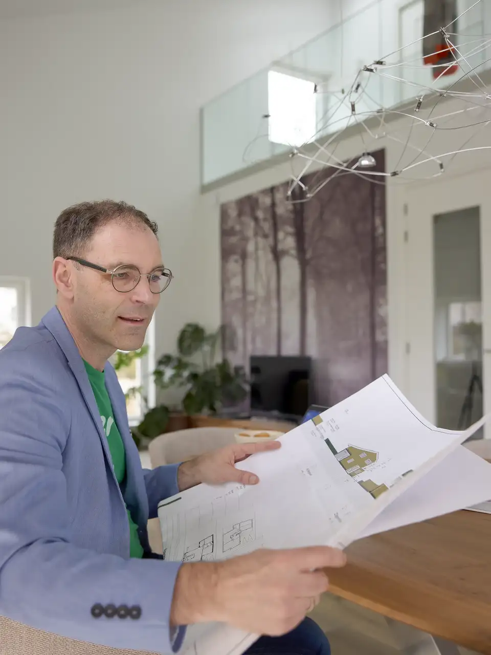 Architect in de woonkamer die onder natuurlijk licht de bouwplannen bekijkt.