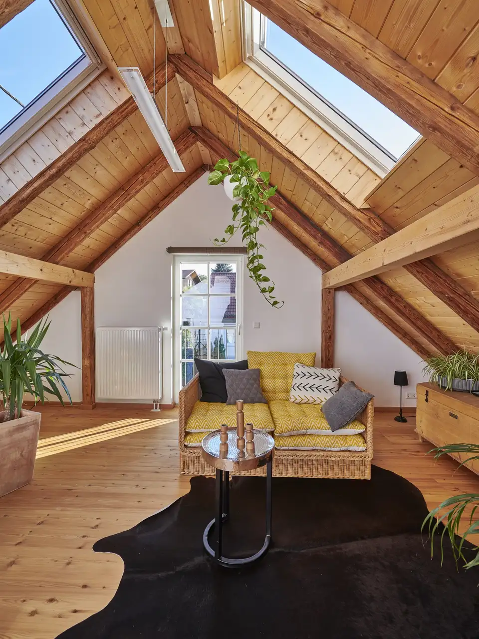 Soggiorno in mansarda con soffitto in legno e grandi finestre per tetti in posizione opposta