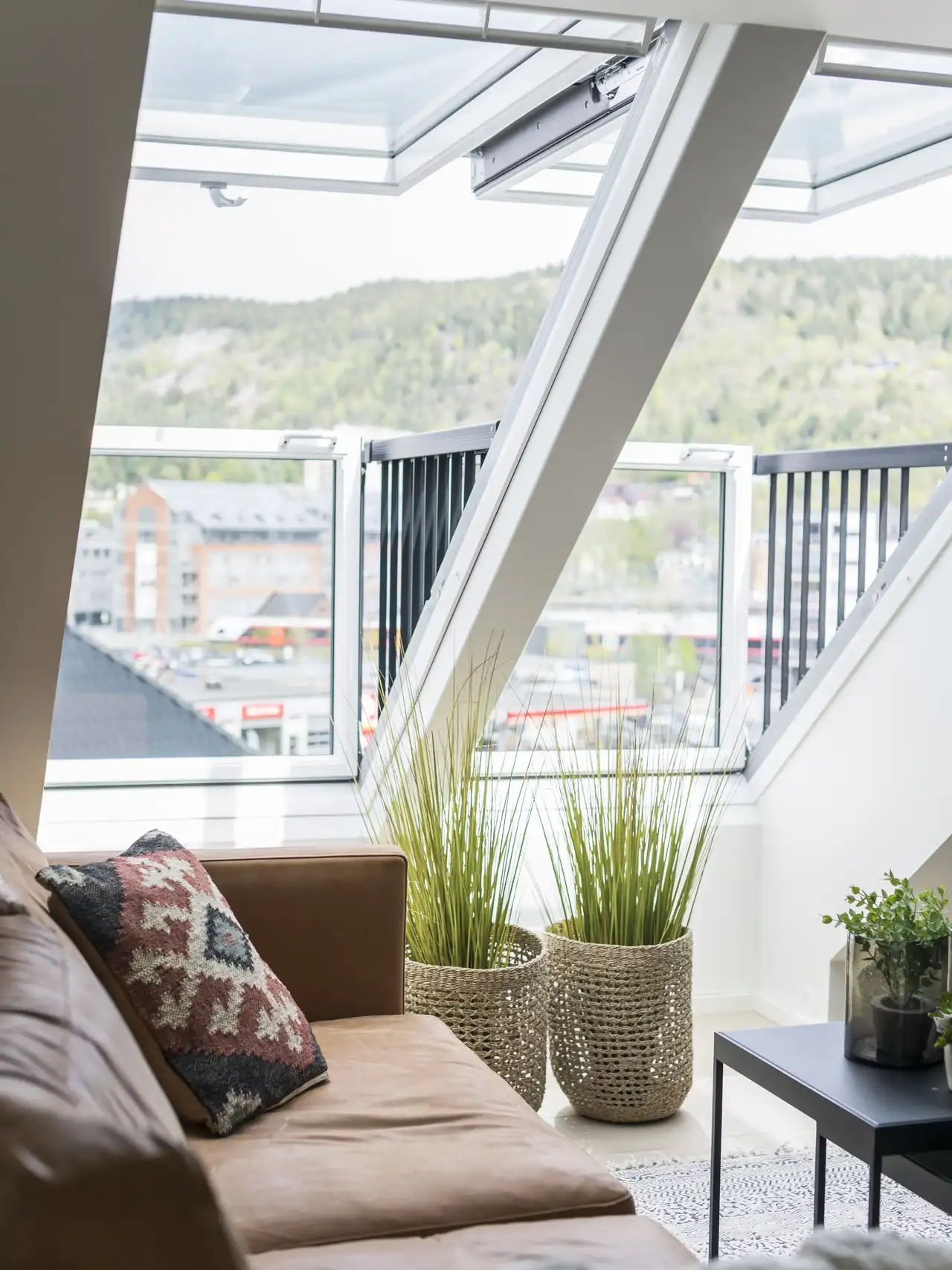 Attic living room with sloped ceiling and open VELUX roof windows, city view.   