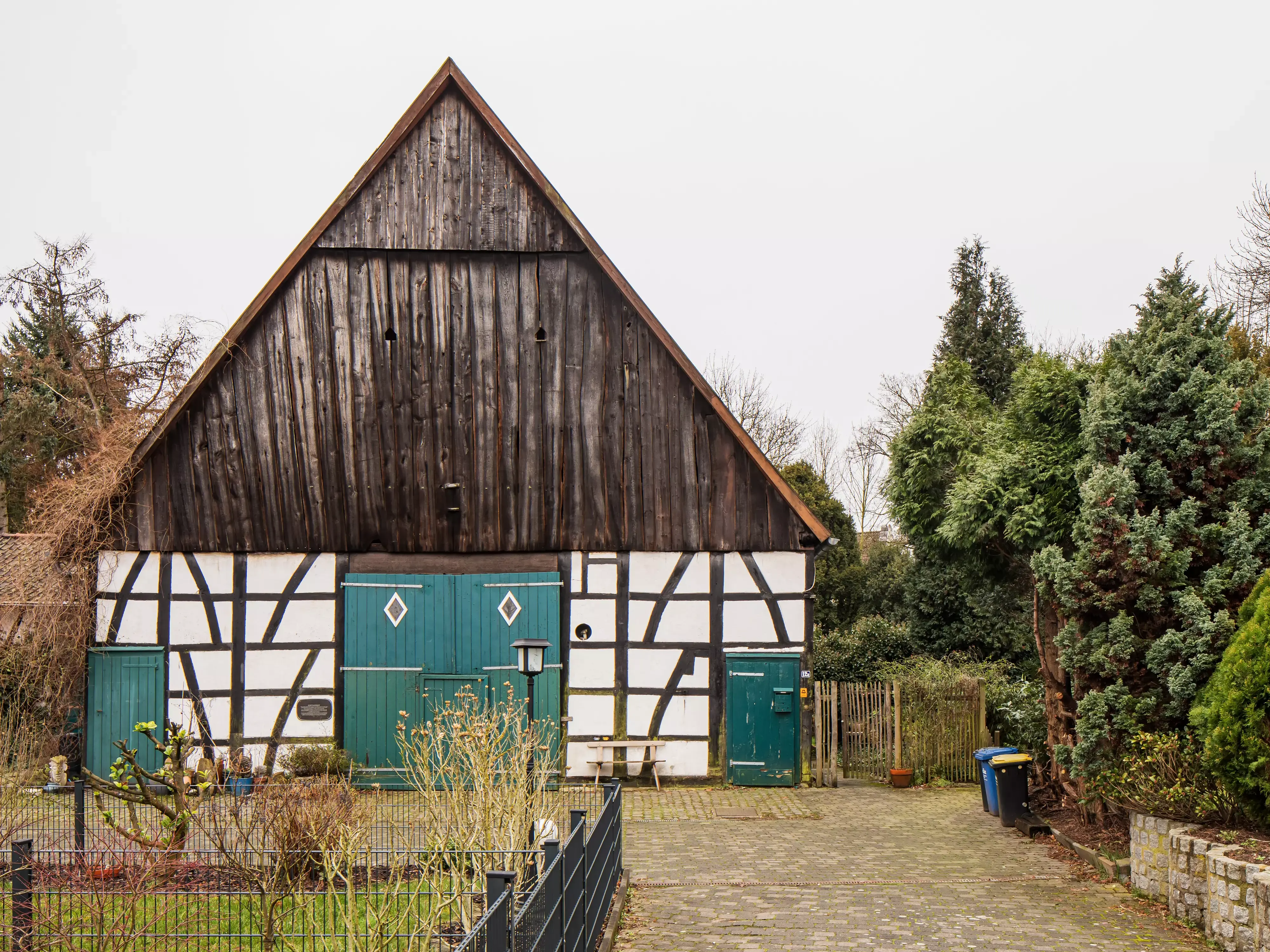 Maison à ossature traditionnelle en bois avec portes vertes et jardin environnant.