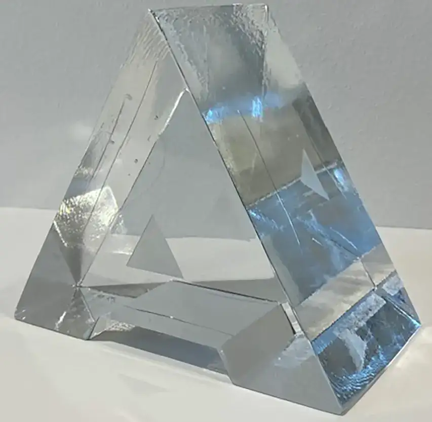 Eine geometrische Glas-Skulptur mit eckigen Formen, die Licht auf einem weißen Sockel reflektiert.