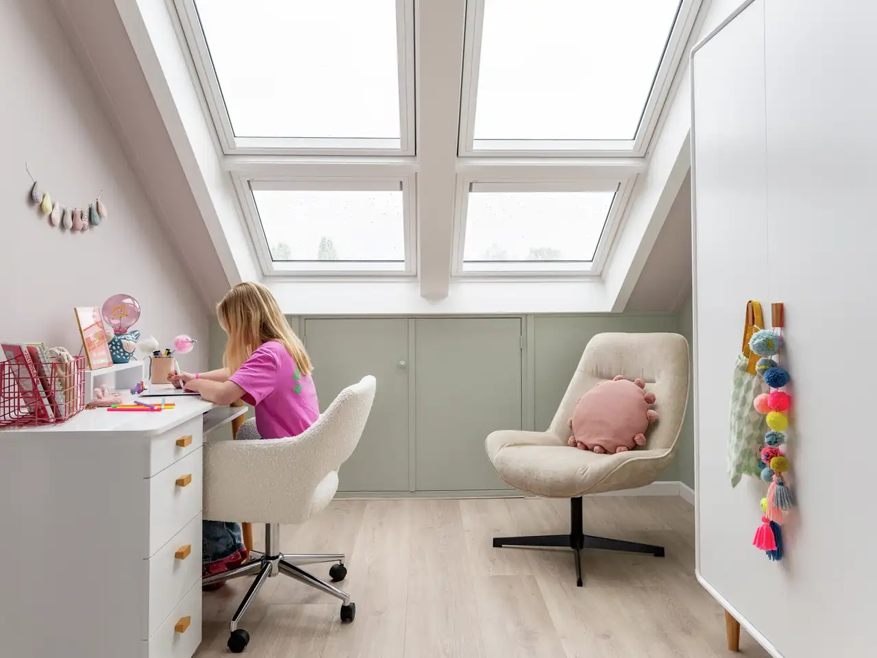 Une enfant fait ses devoirs à son bureau près de grandes fenêtres de toit VELUX 