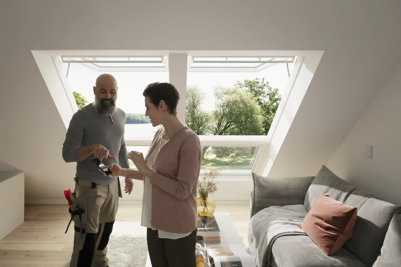 Rozprávajú sa žena a inštalatér VELUX s veľkými strešnými oknami VELUX za nimi.