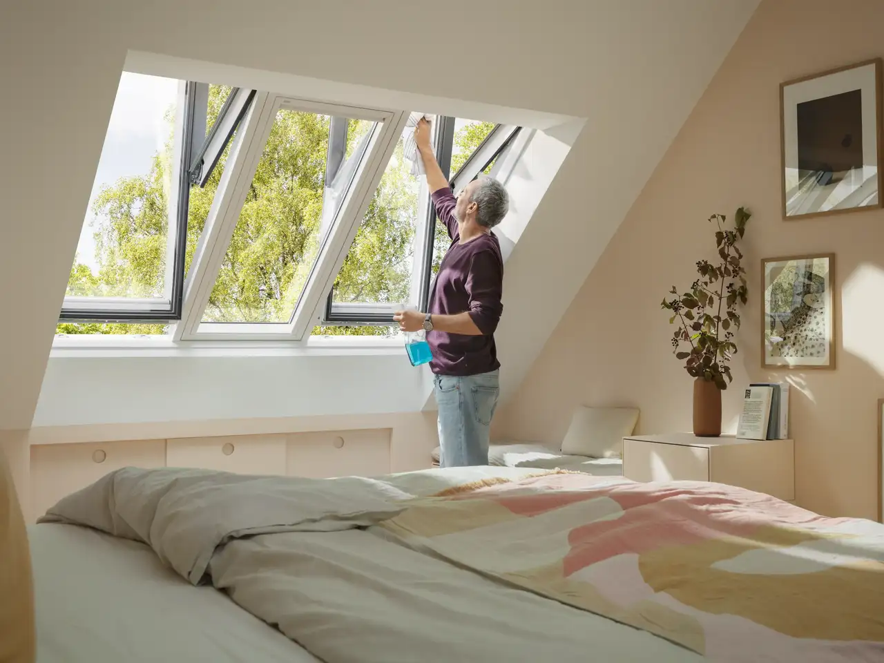 Älterer Mann mit Putzmittel in der einen und Lappen in der anderen Hand beim Dachfensterputzen | VELUX Magazin