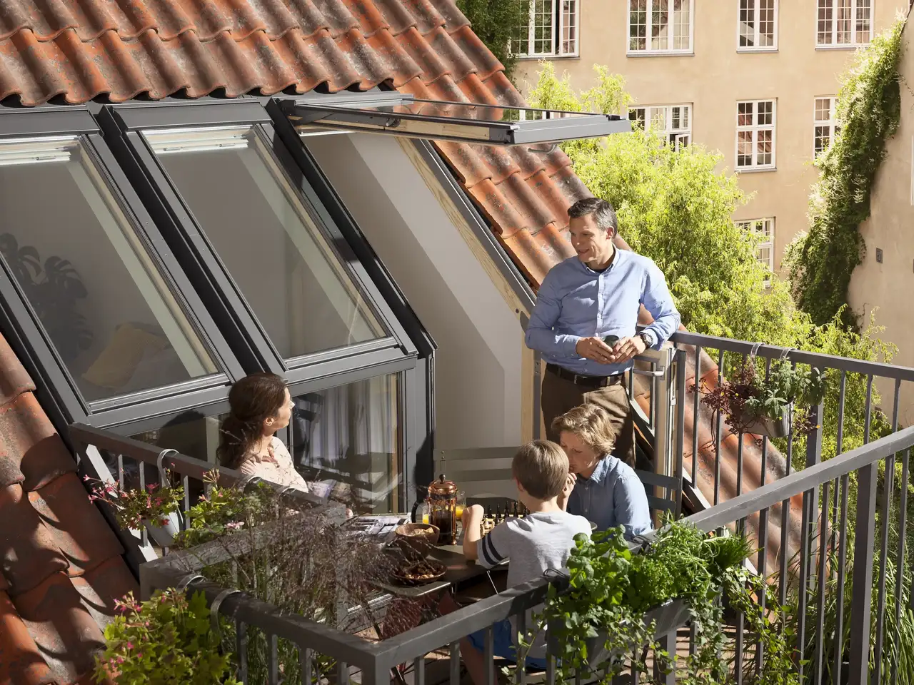 La famiglia siede insieme sul balcone sul tetto e si gode la vacanza a casa propria | Rivista VELUX