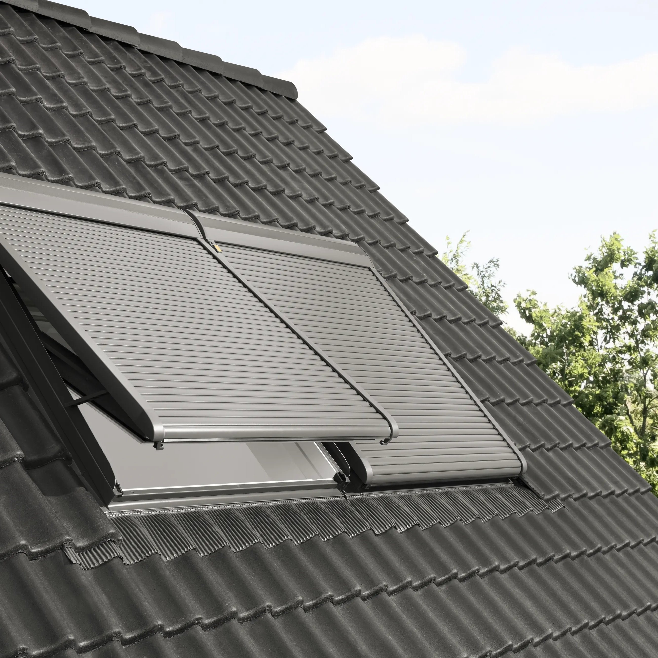 Modern roof with dark tiles and partially open VELUX roof window.