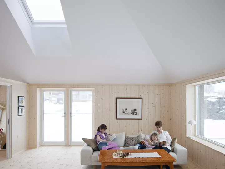 Helles Wohnzimmer mit VELUX Dachflächenfenster, hölzernen Wänden und verschneiter Aussicht draußen.