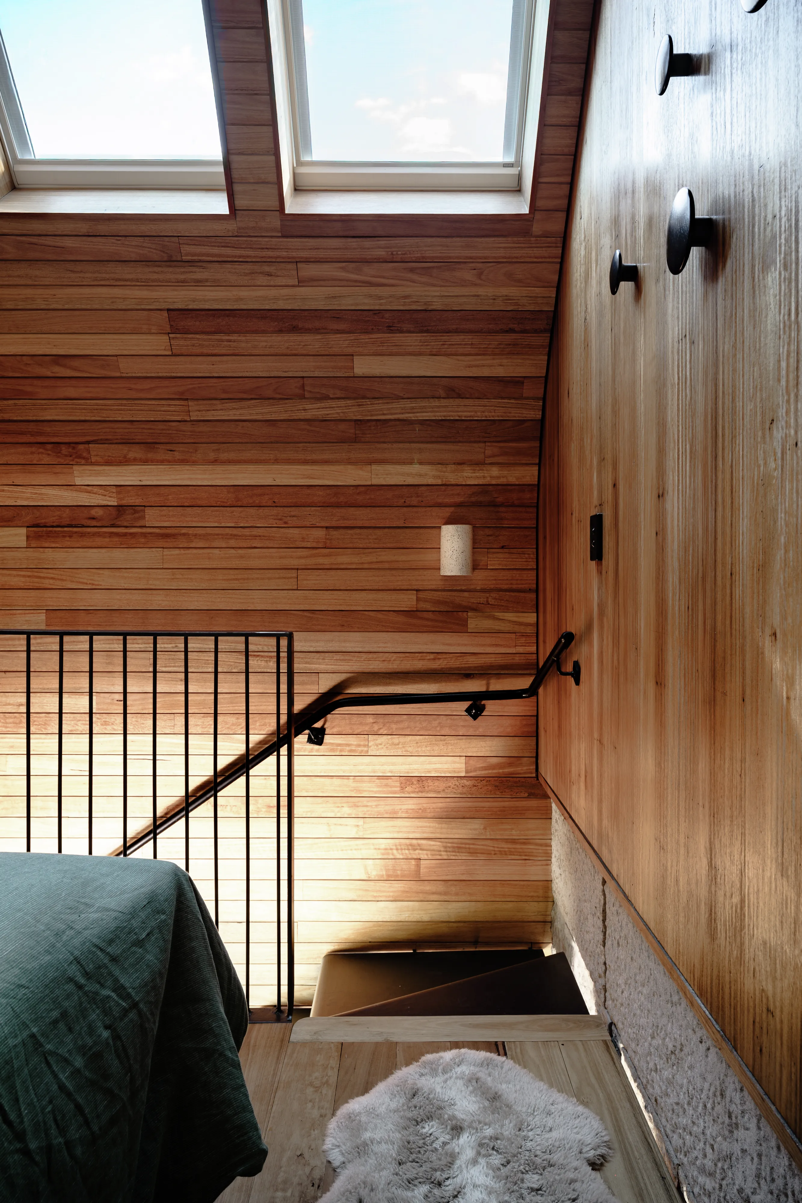 Wood-clad attic stair area lit by two VELUX roof windows above a cozy bedroom corner.