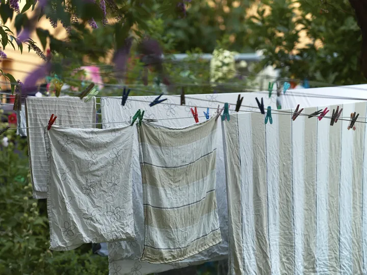 Beige-weiß gestreifte Bettwäsche und Handtücher hängen draußen im Grünen auf einer Wäscheleine | VELUX Magazin