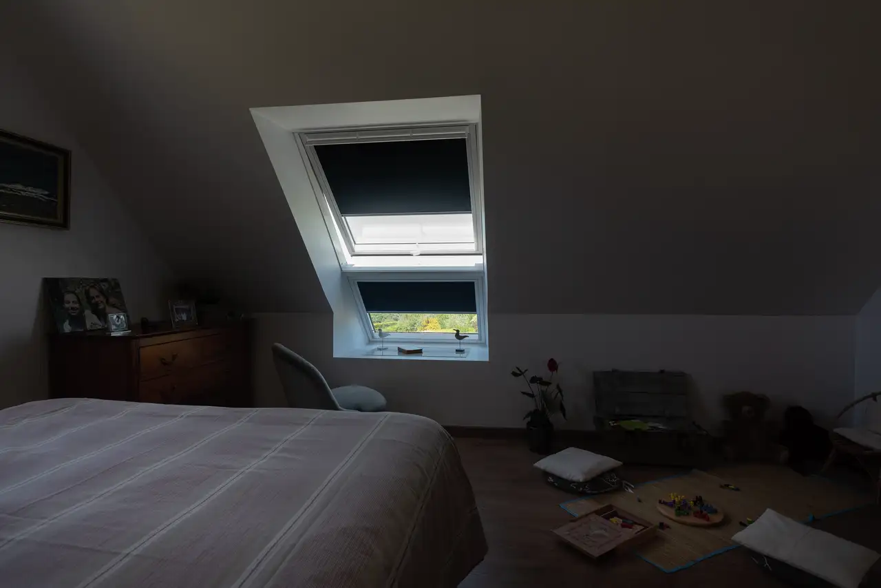 Chambre mansardée avec verrière plane VELUX équipée de stores occultants.