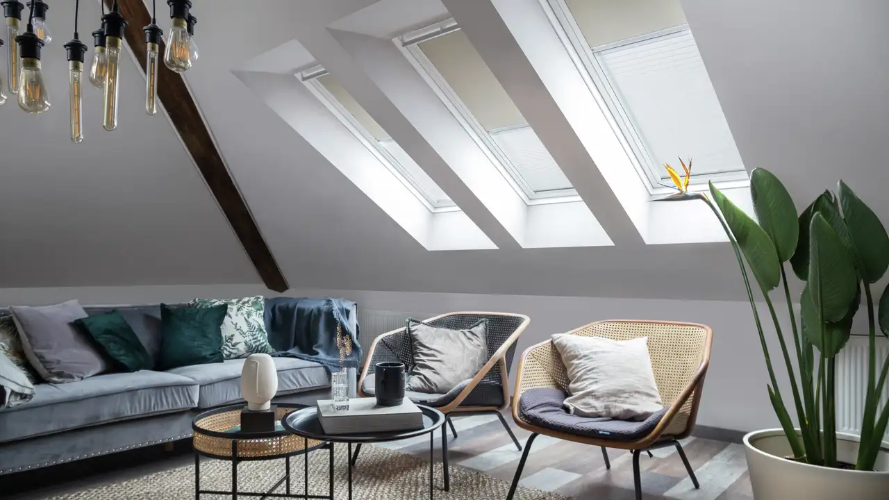Séjour avec détails rétro : assises en rotin, coussins aux motifs variés et trois fenêtres de toit VELUX alignées.
