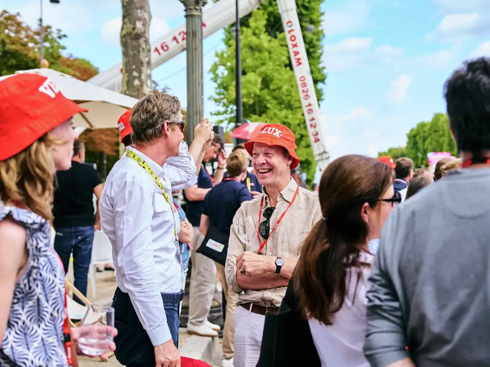 Množica na zunanjem dogodku Tour de France, ki ga je gostil VELUX, mnogi z rdečimi klobuki, pod jasnim nebom.