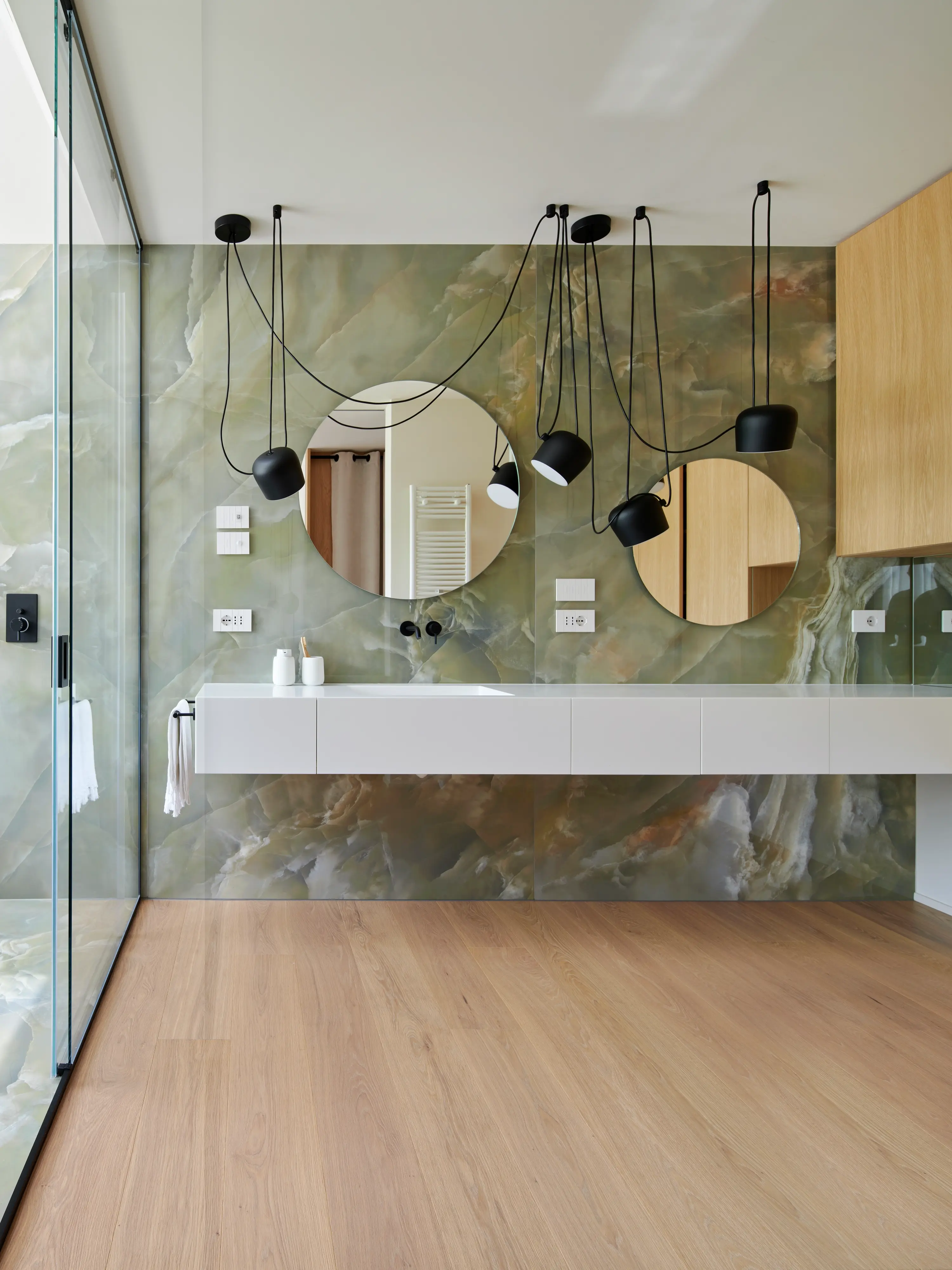 Salle de bain contemporaine avec des murs en marbre, des armoires en bois et des miroirs circulaires.