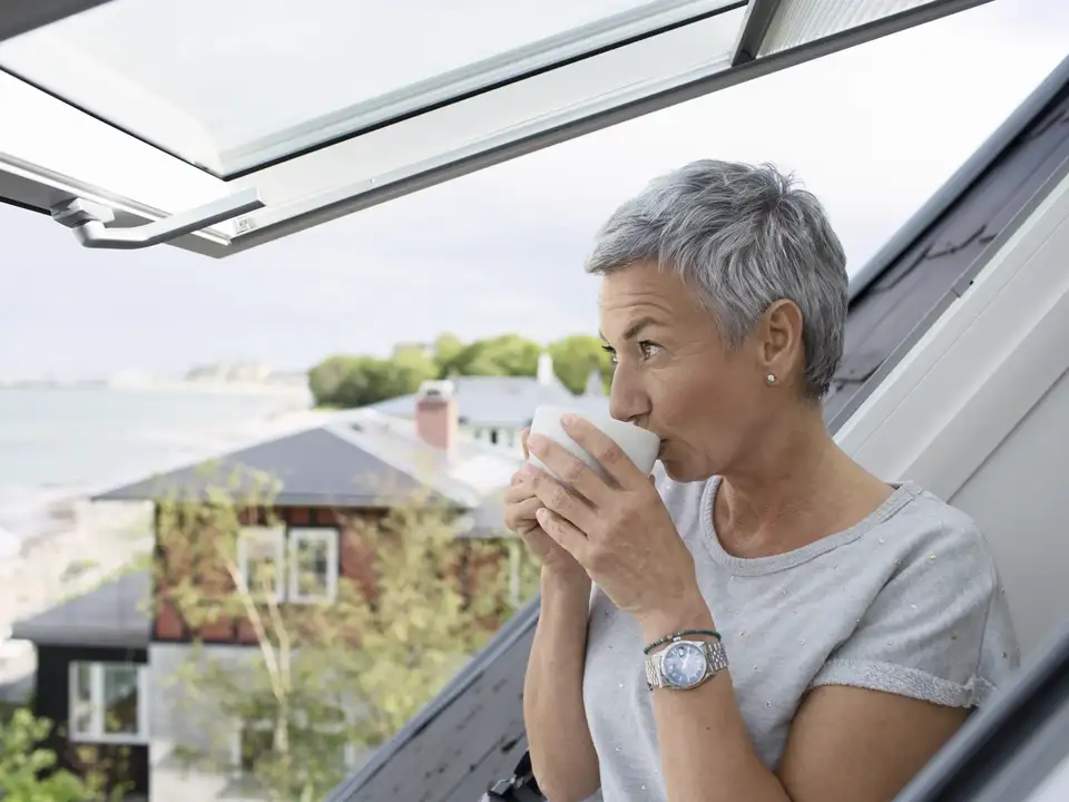 Kvinde nyder udsigten og en kop kaffe ved åbent tagvindue med havudsigt