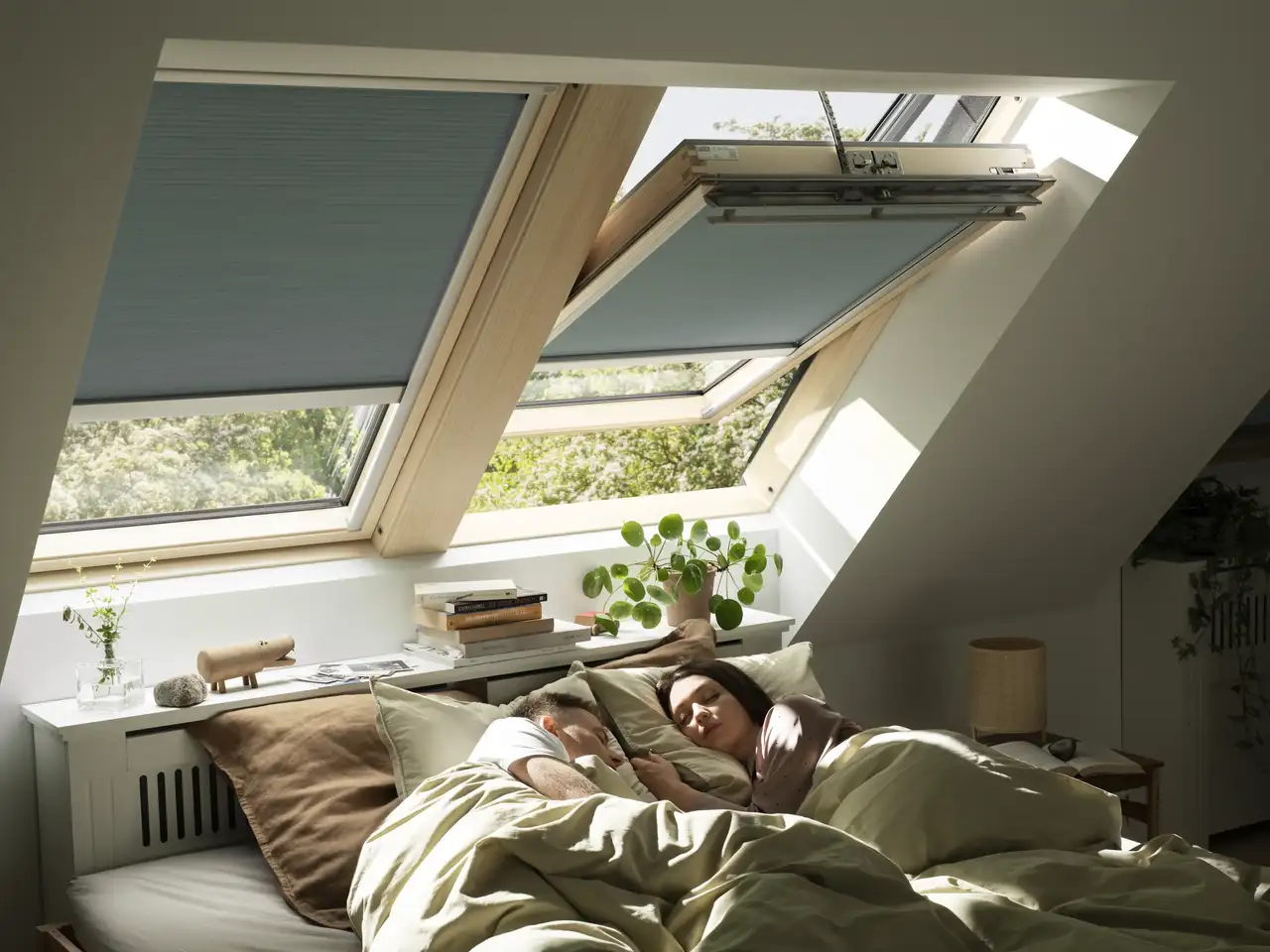 Una pareja duerme en la cama bajo dos ventanas de tejado con cortinas de oscurecimiento.
