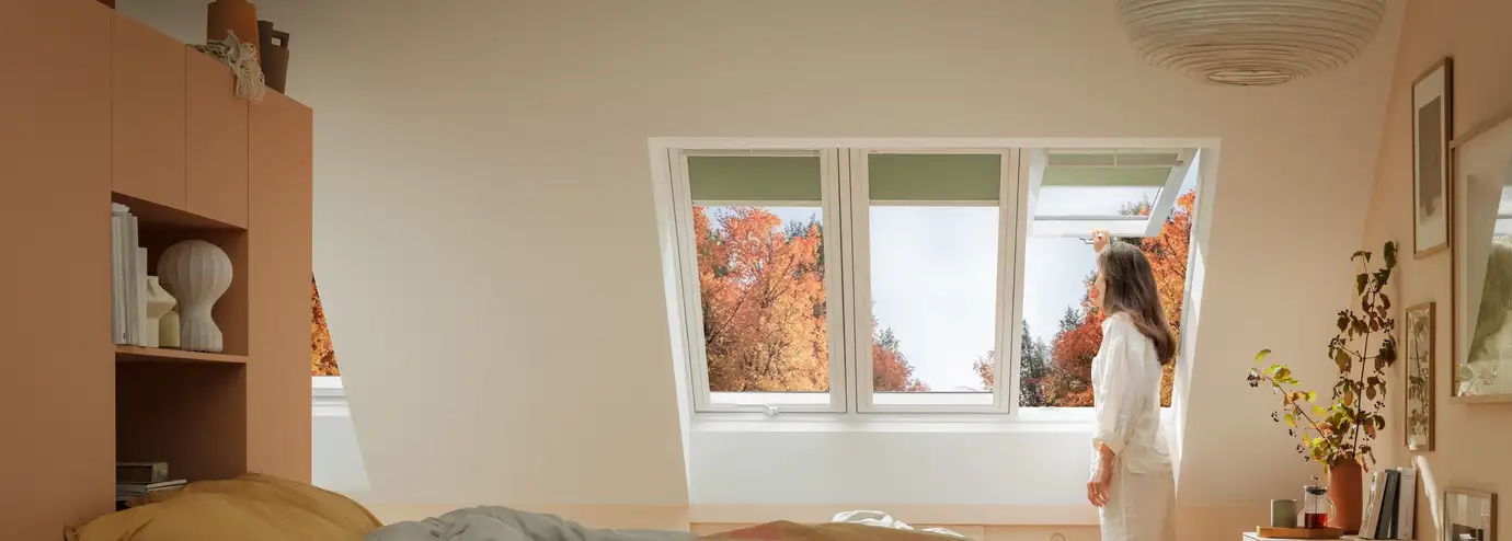 Attic bedroom with VELUX roof window, autumn view, woman standing.