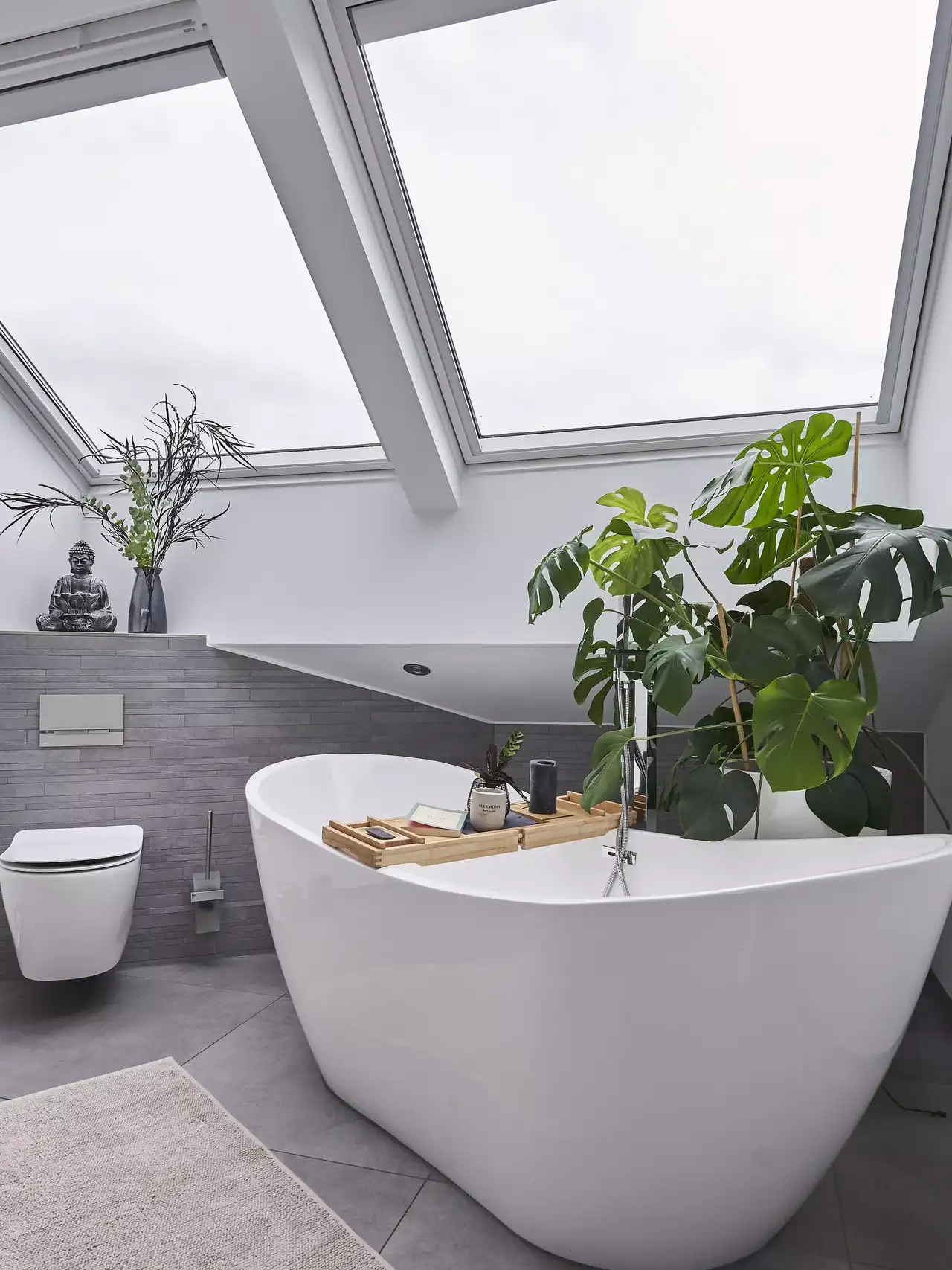 Modernes Badezimmer mit freistehender Badewanne, VELUX Dachflächenfenster und grünen Pflanzen.