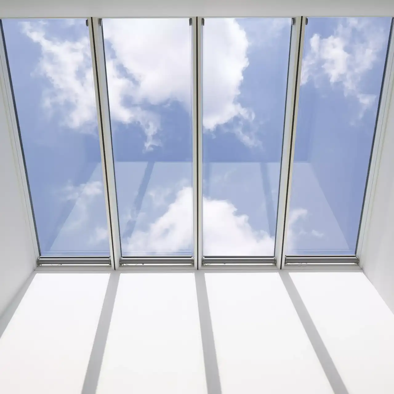 Innenansicht eines VELUX Dachflächenfensters mit blauem Himmel und Wolken, die sich spiegeln.