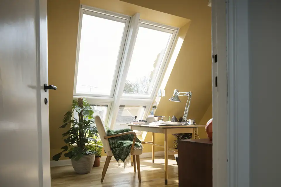 Studio in mansarda con soffitto inclinato dipinto di giallo e finestra per tetti che illumina la scrivania