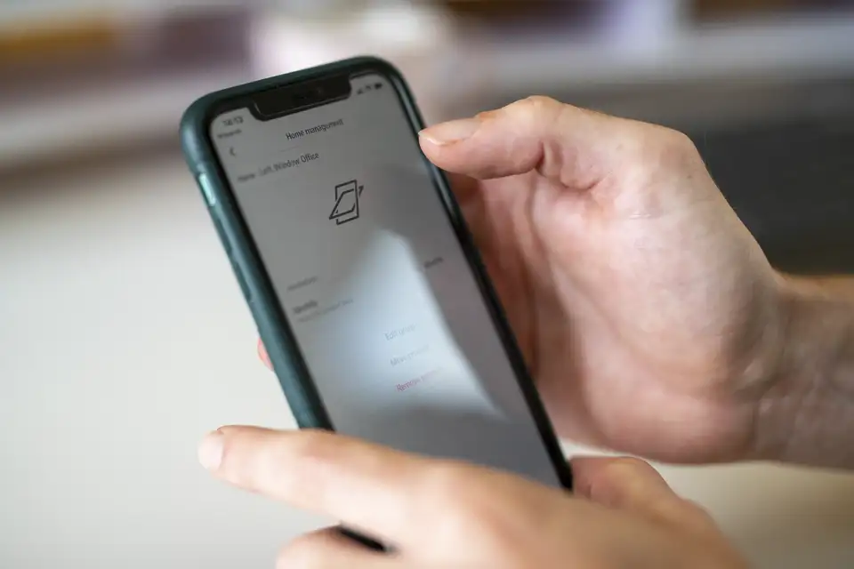 VELUX uygulamasını gösteren bir akıllı telefonu tutan elin yakın çekimi; çatı pencerelerini uzaktan kontrol etmek için kullanılıyor | VELUX.