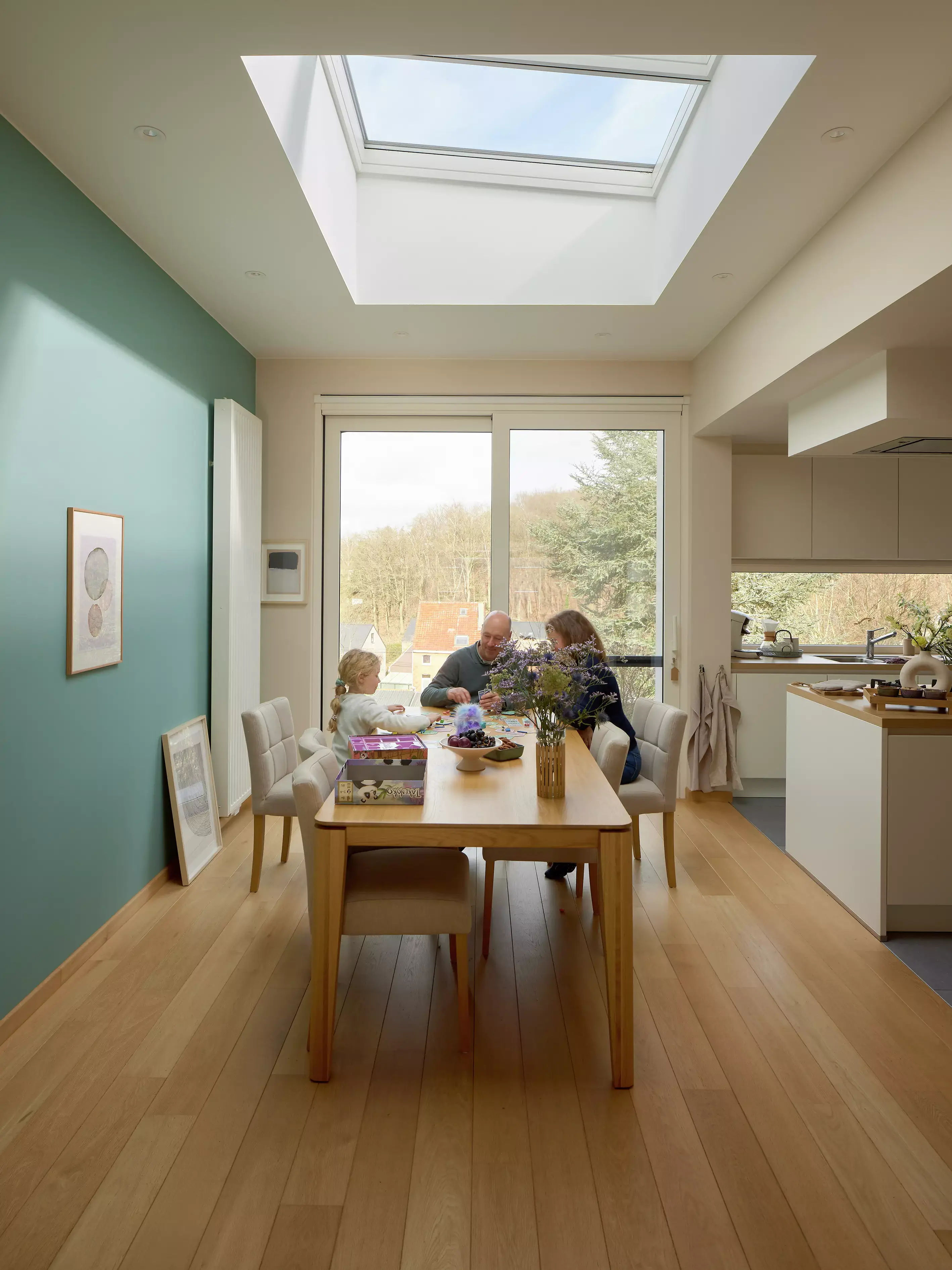 Espace salle à manger ouvert avec lumière naturelle provenant d'une fenêtre de toit VELUX, table en bois et cuisine ouverte.