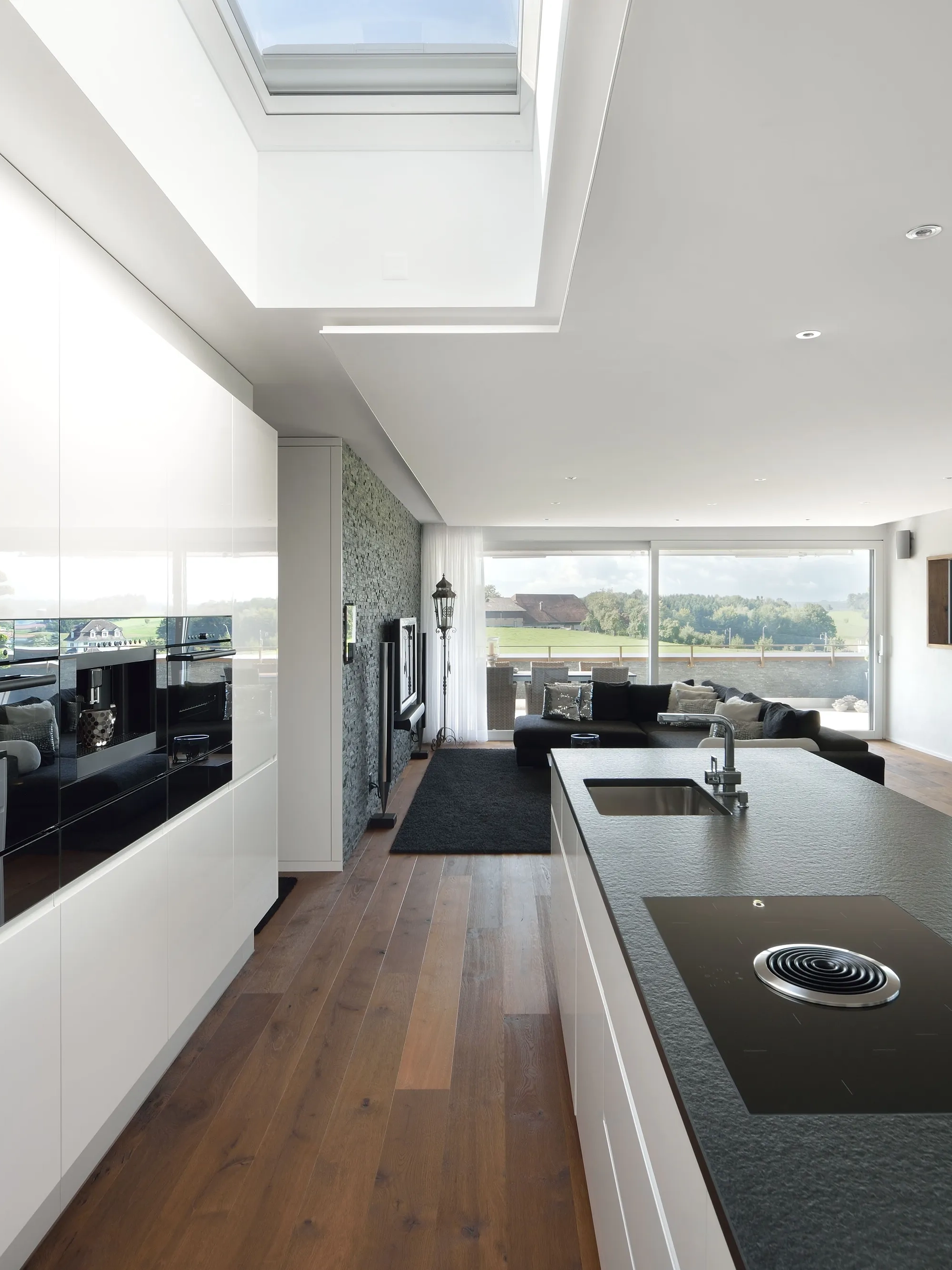 Cucina moderna con finestra da tetto VELUX, mobili bianchi e pavimento in legno.