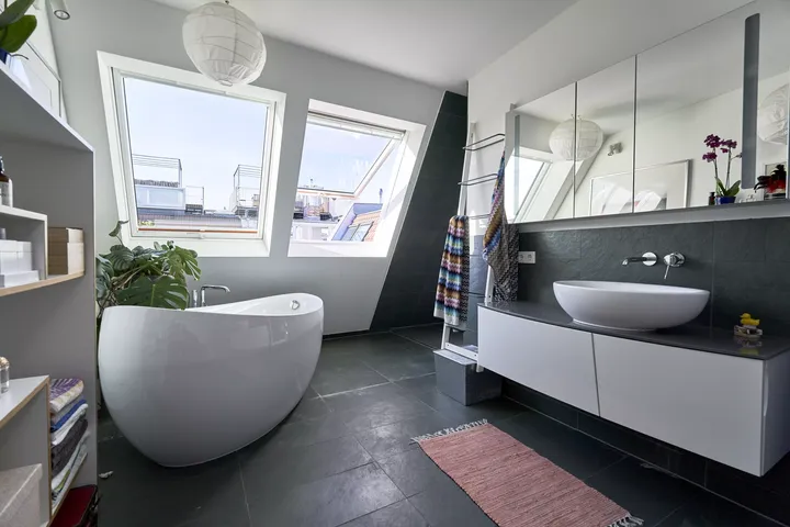 Modernes Badezimmer mit VELUX Dachflächenfenster, freistehender Badewanne und dunklen Fliesen.