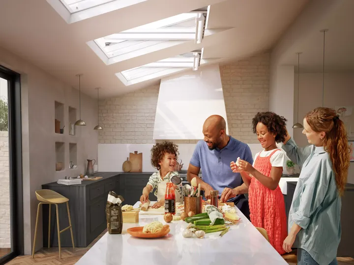 Moderne, sonnendurchflutete Küche mit kochender Familie, VELUX-Fenster darüber.