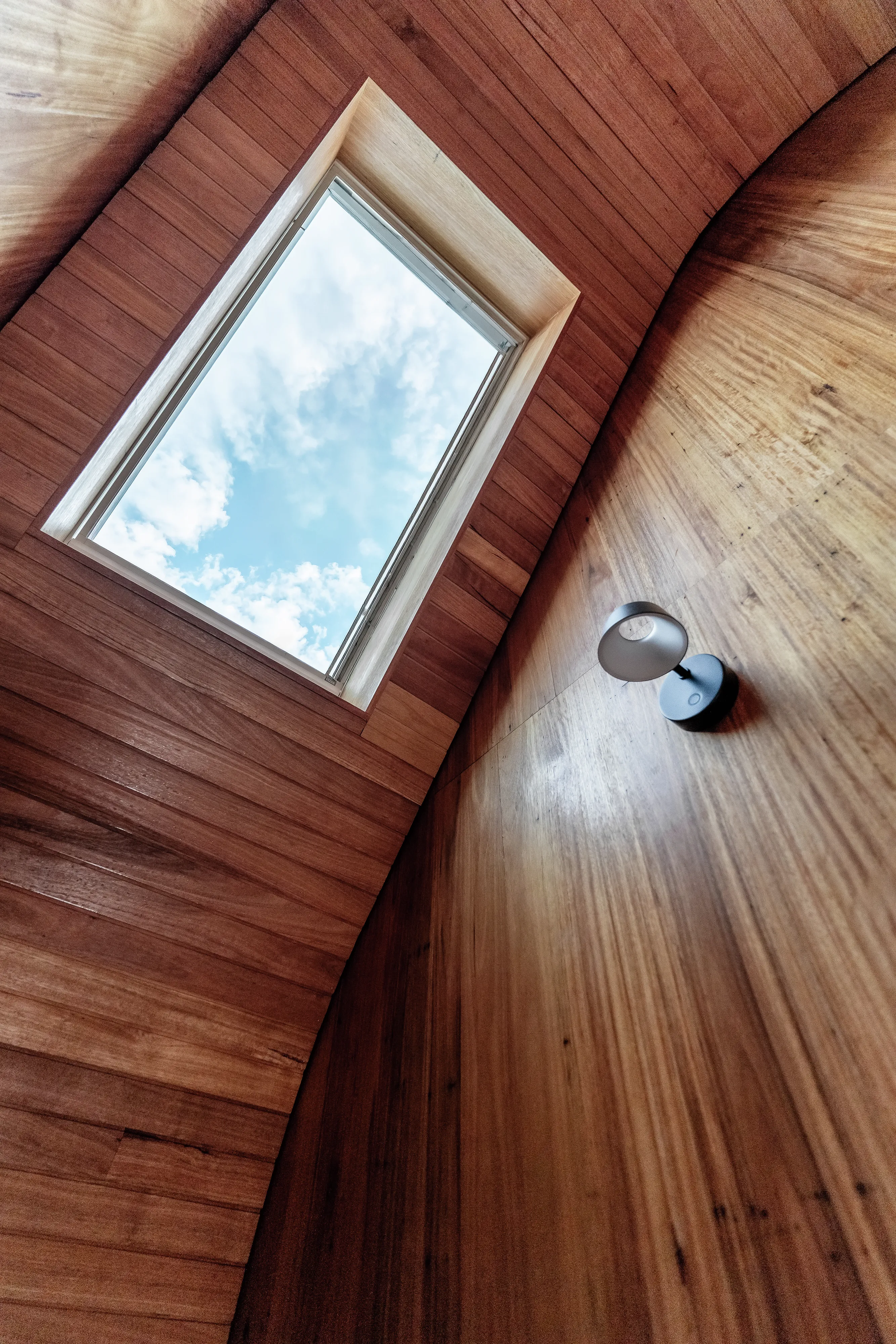 Sloped wooden ceiling with VELUX roof window and small wall light, blue sky visible.
