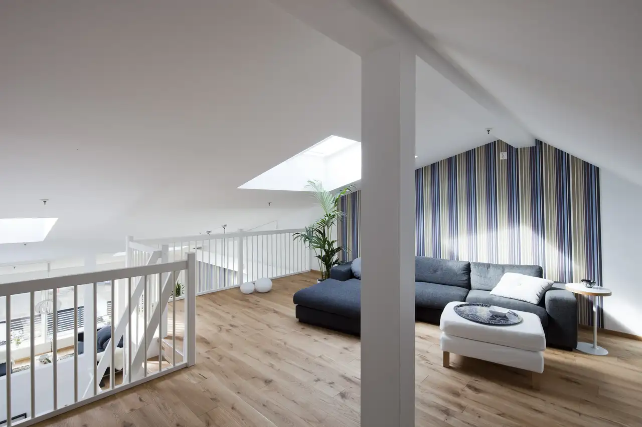 Salon mansardé avec plafond et murs blancs, et une seule paroi décorée de papier peint à motif vertical