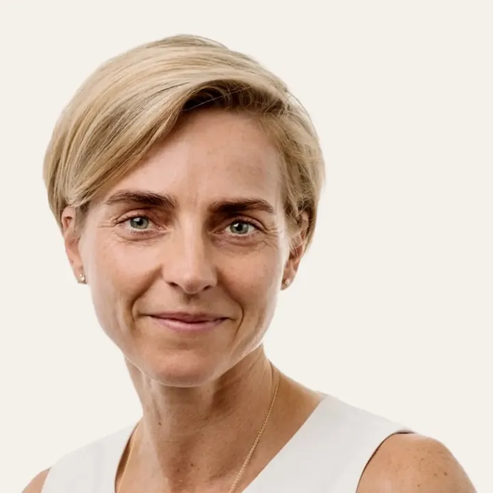Woman with short blonde hair in a white sleeveless top and gold necklace.