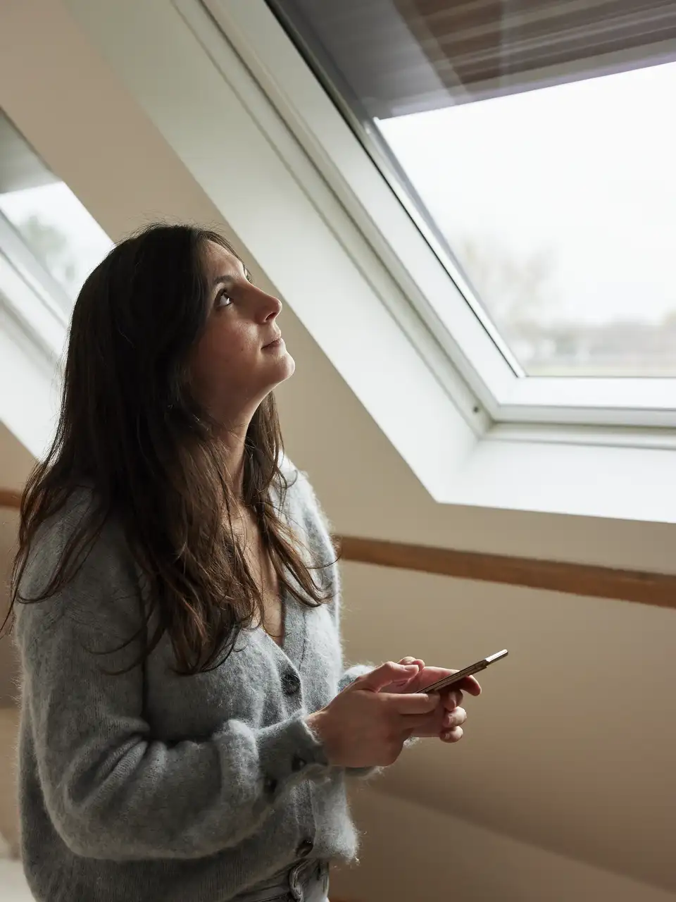 Een vrouw laat het rolluik van een VELUX dakvenster zakken.