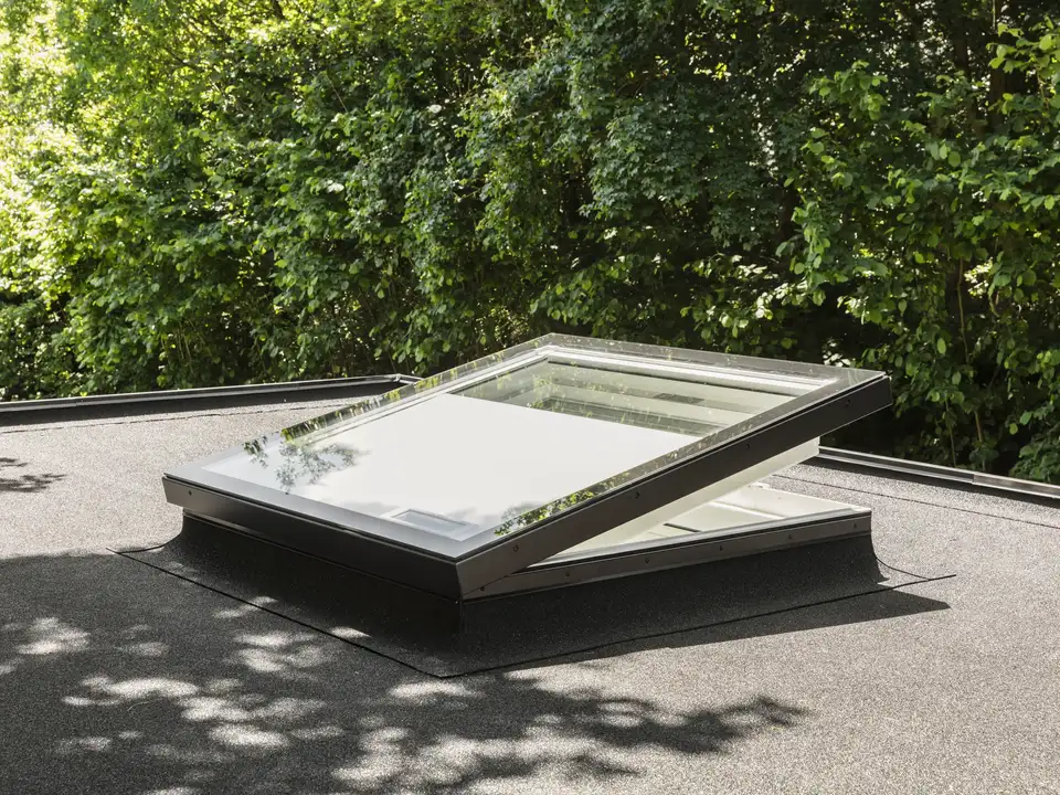Finestra per tetti piani VELUX aperta, circondata da verde.