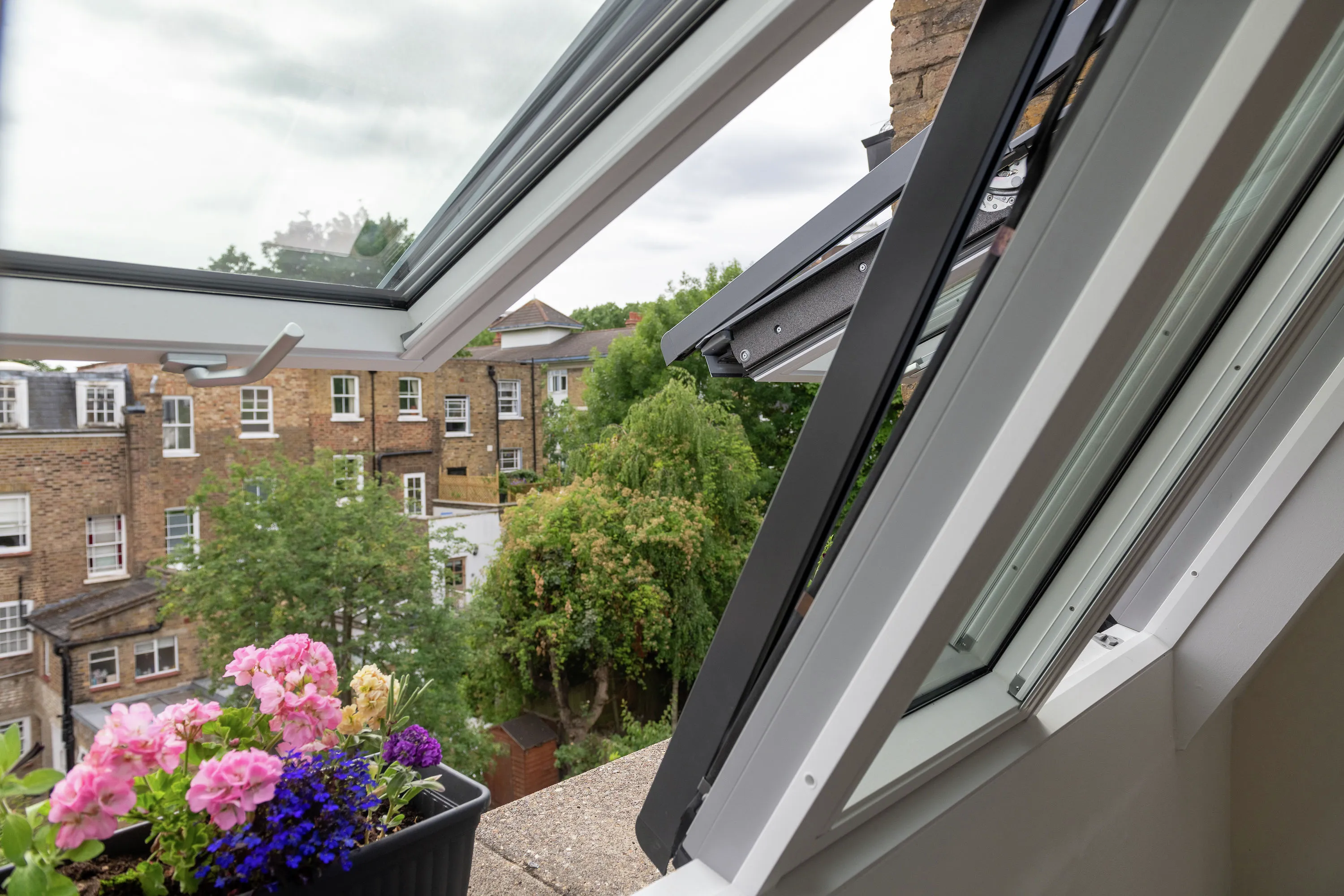 Open VELUX roof window with view of terraced houses and flowers.