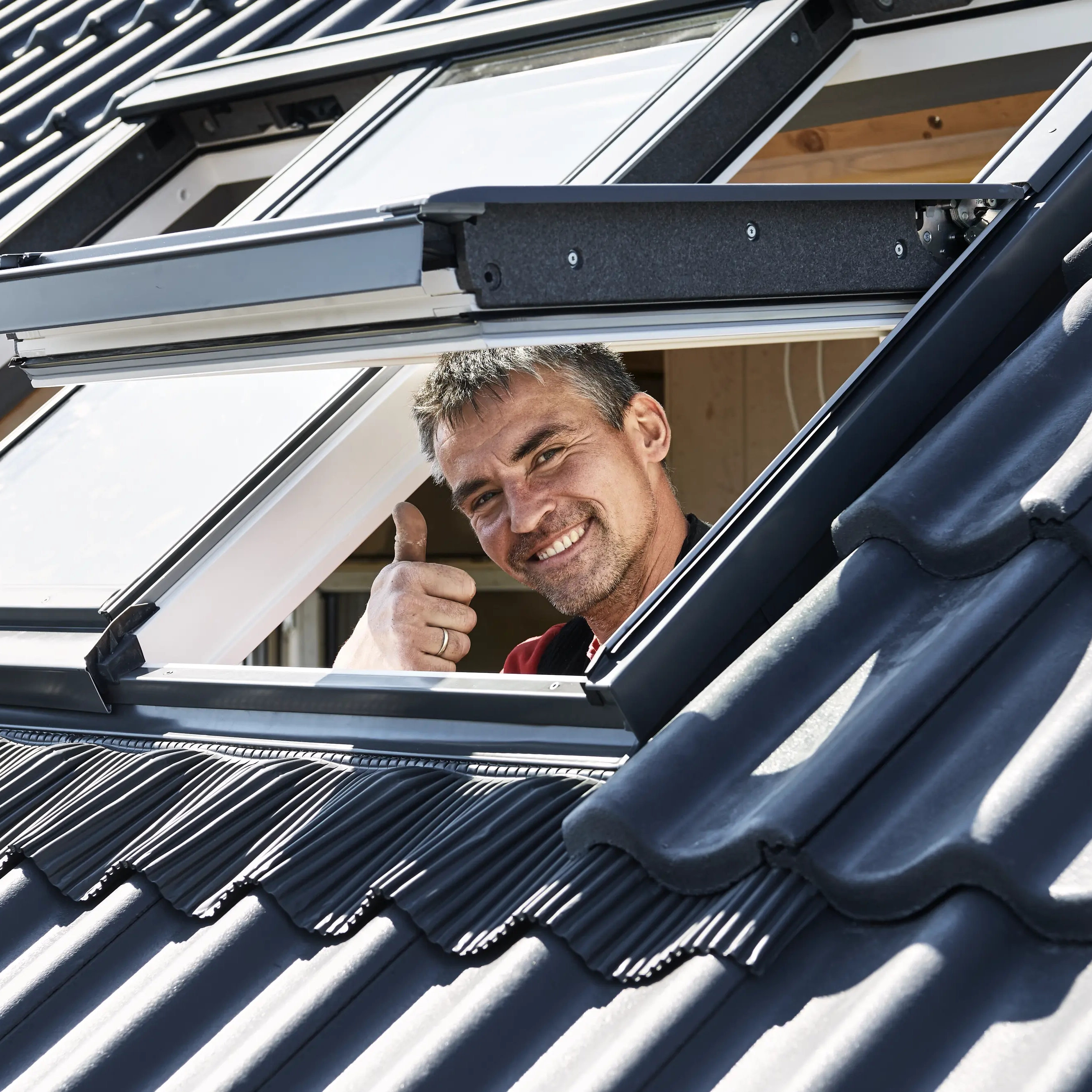 Open VELUX roof window on a tiled roof, allowing light and air inside.