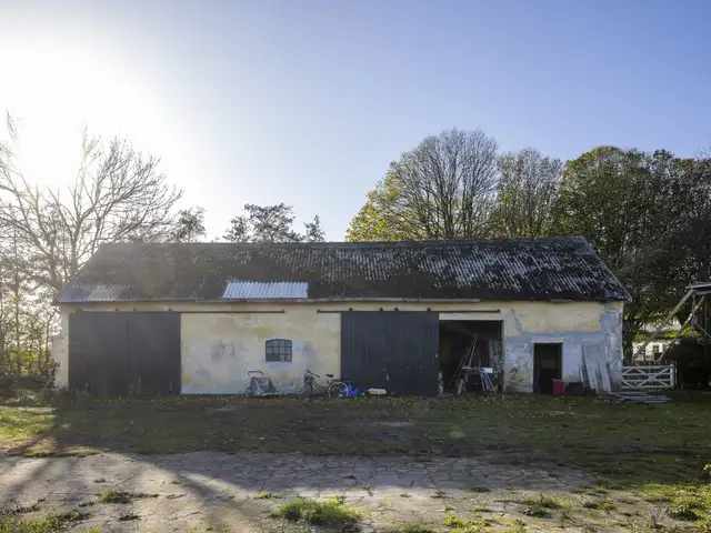 Gammel lade med slidt og forvitret eternittag omgivet af åben plads