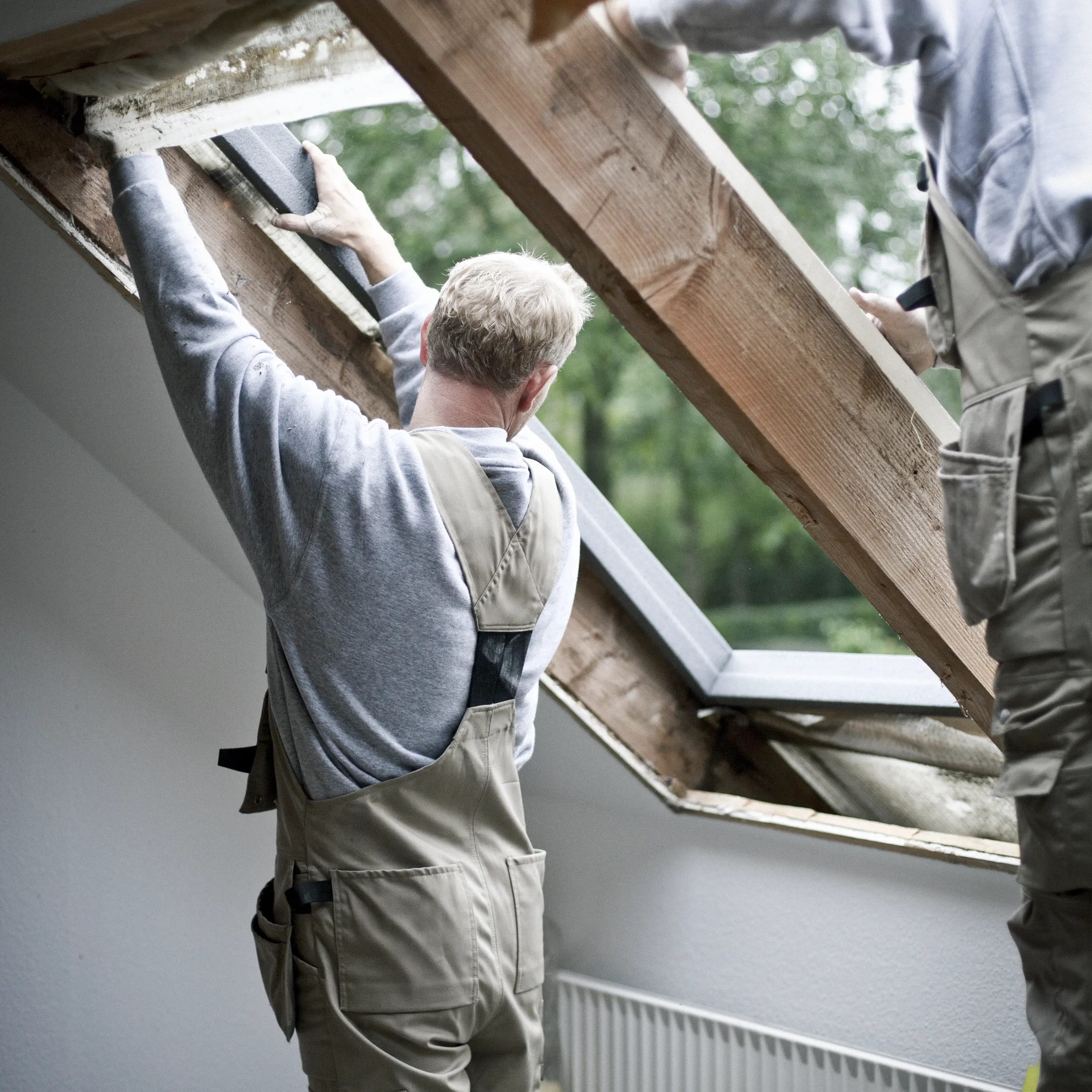 Workers installing VELUX roof window in attic with sloped ceiling.