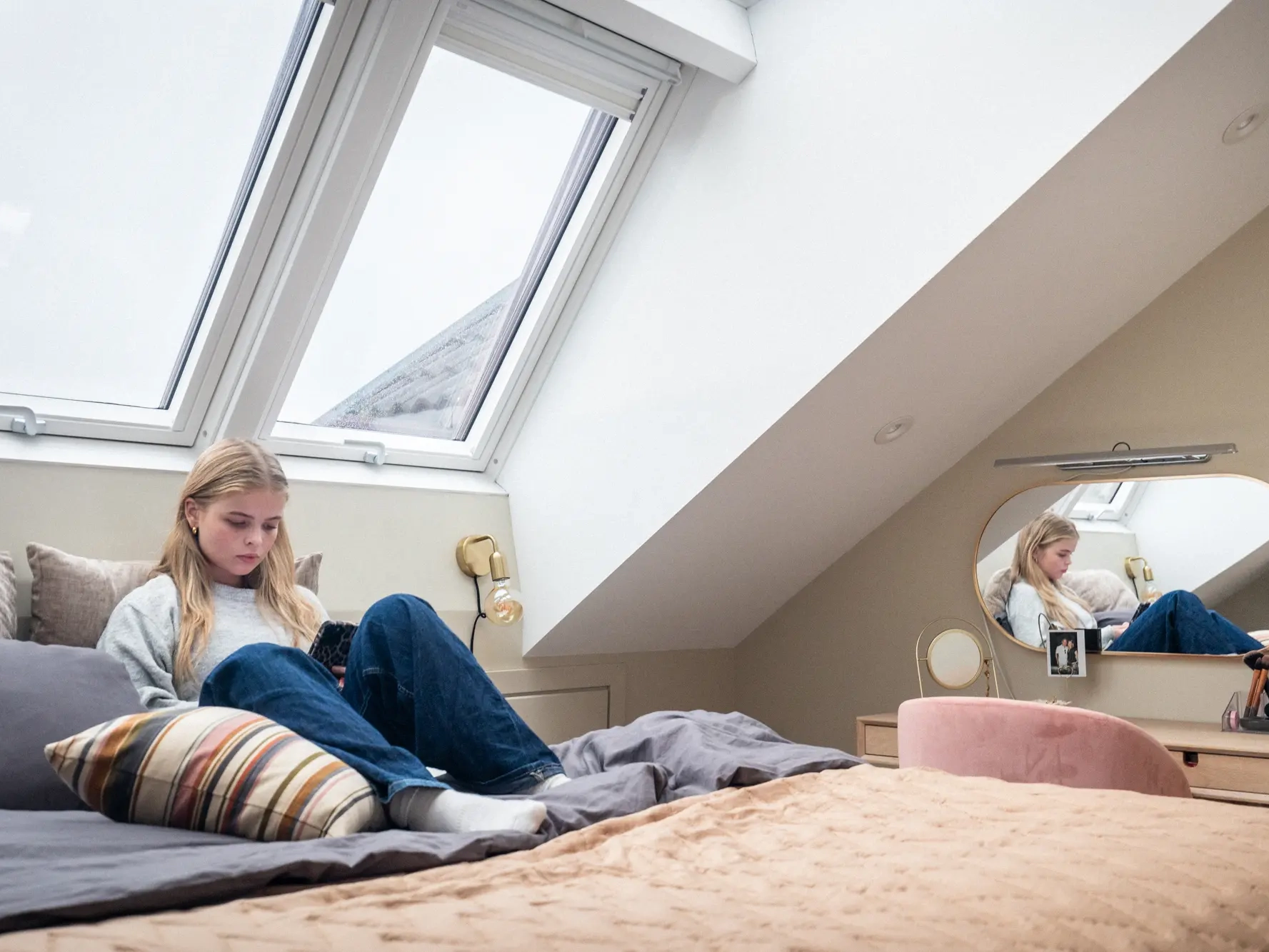 Una ragazza legge sul suo letto sotto due finestre per tetti VELUX affiancate