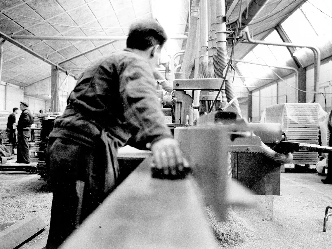 Ouvrier manipulant des machines dans un atelier d'usinage du bois industriel animé avec de la sciure visible.