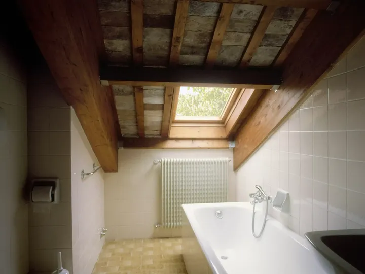 Rustikales Badezimmer mit freiliegenden Balken und einem VELUX Dachflächenfenster über der Badewanne.