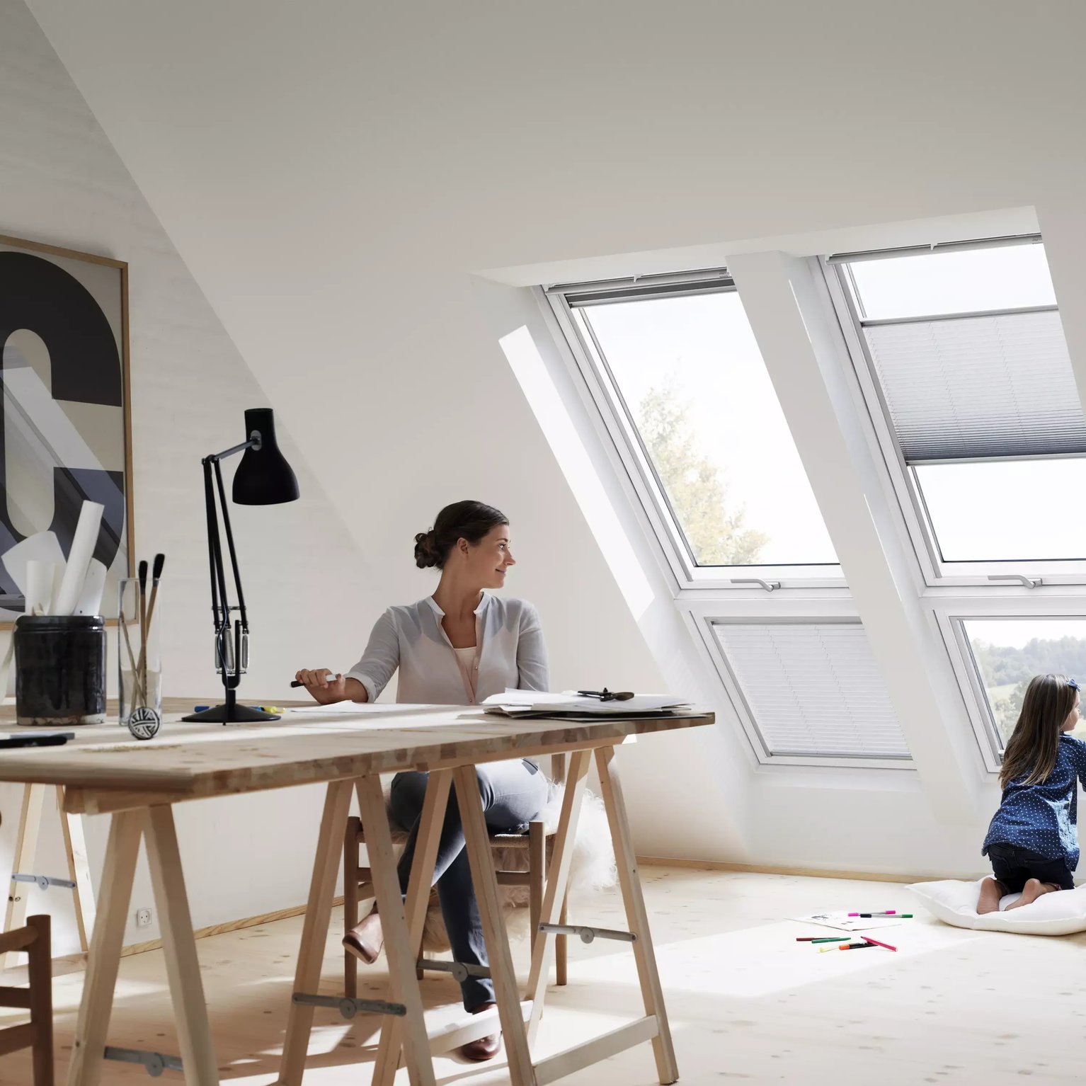 Attic workspace with sloped ceiling and VELUX roof windows, child looking outside.