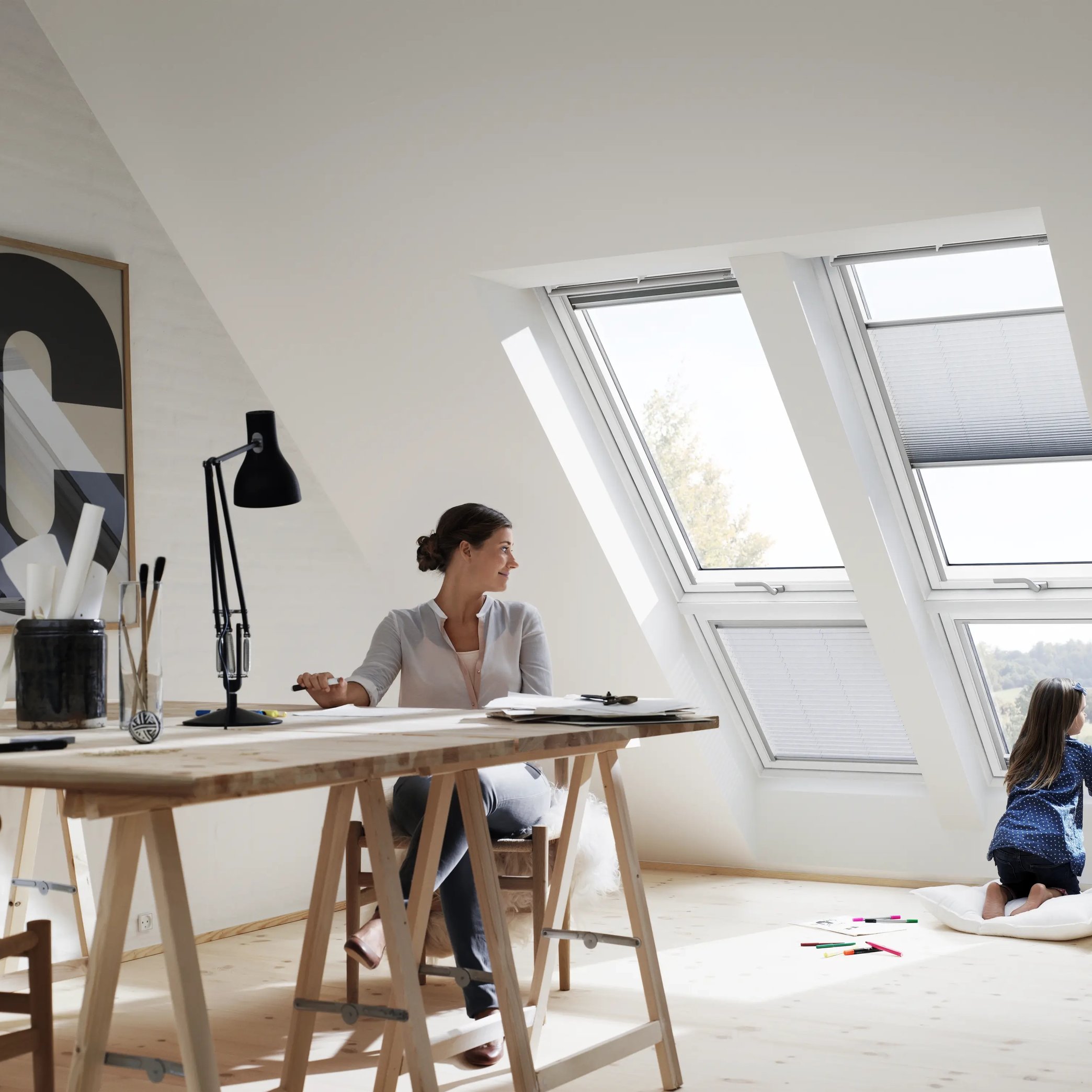 Attic workspace with sloped ceiling and VELUX roof windows, child looking outside.