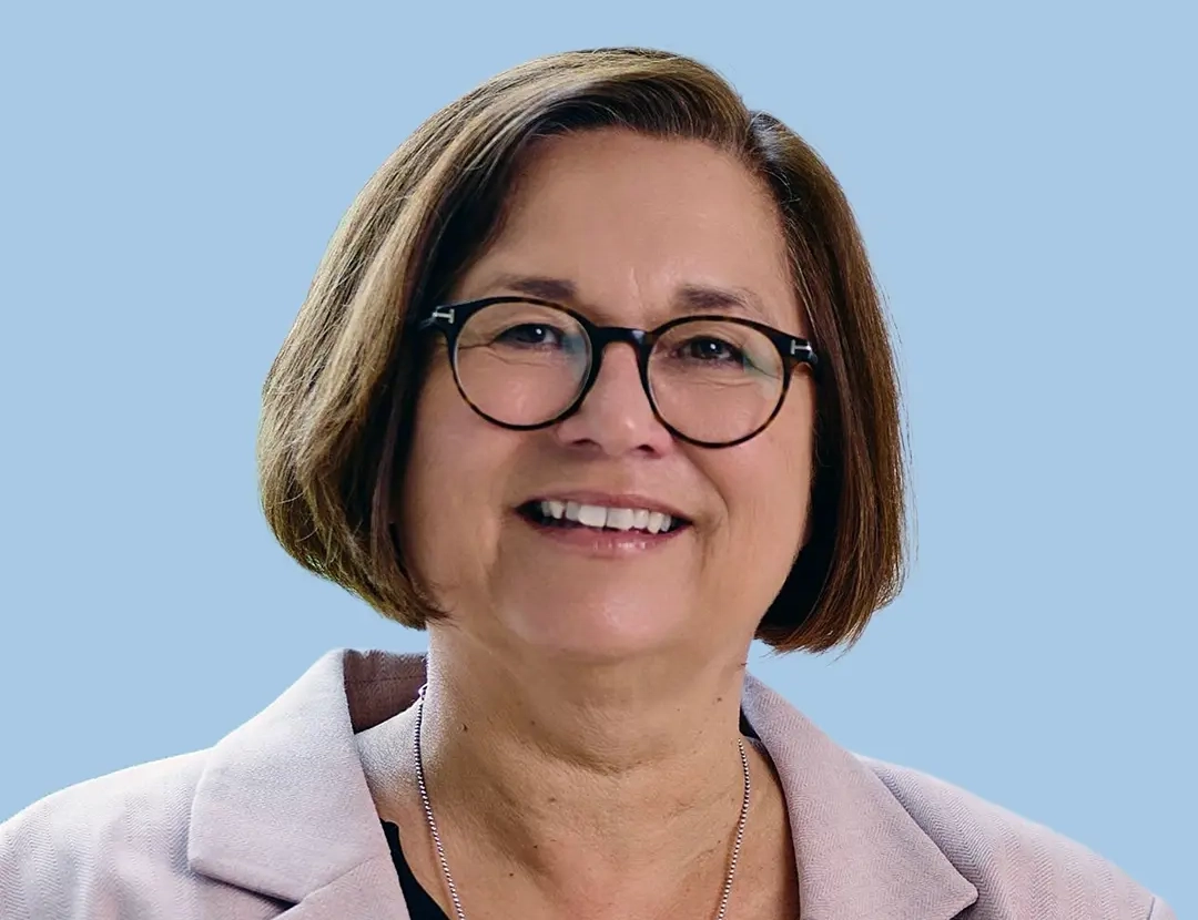 Woman in pastel pink blazer with silver necklace, light blue background.
