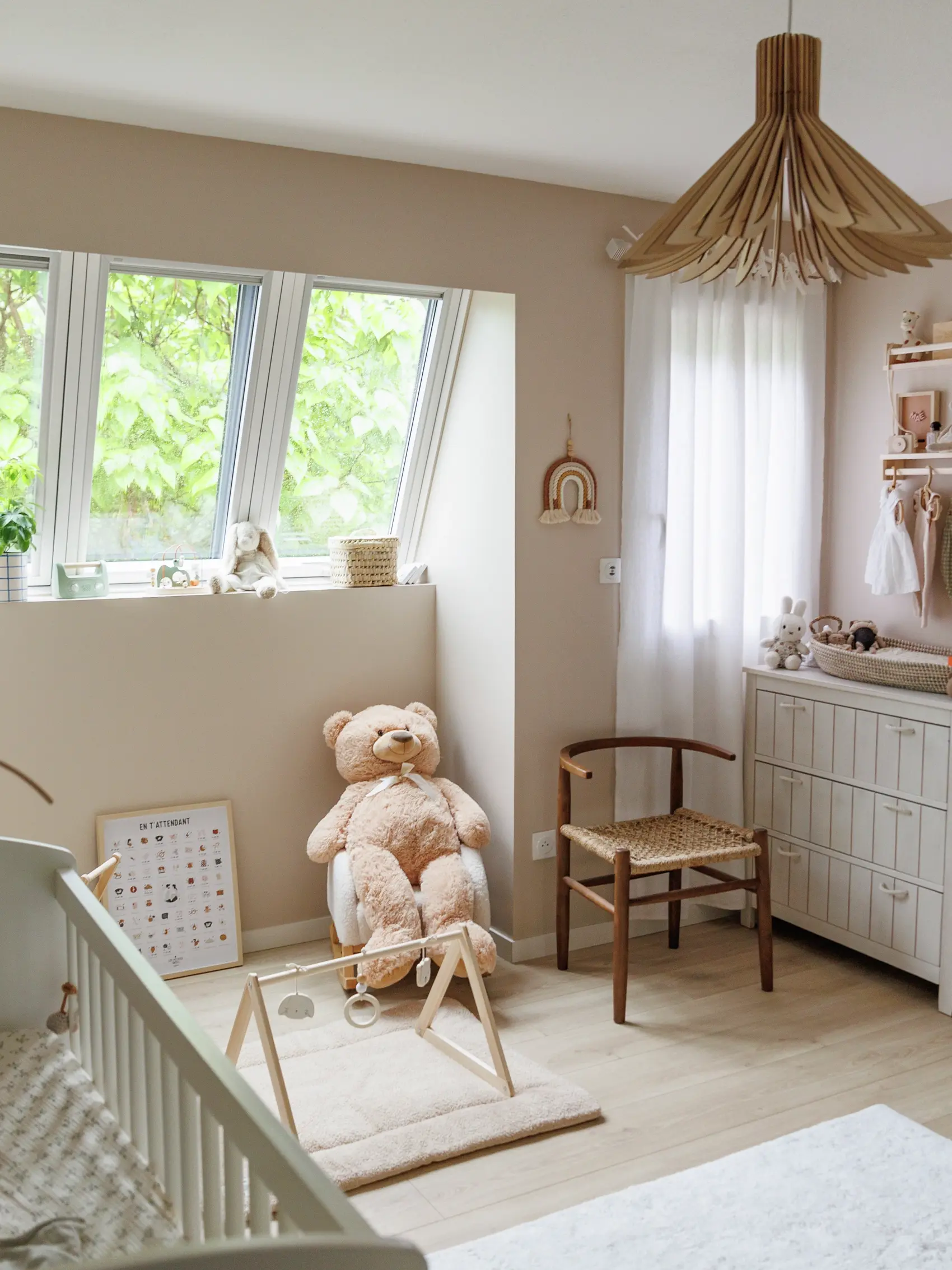 Chambre d'enfants confortable avec un ours en peluche sur une balançoire, décor en bois et une vue sur la verdure à l'extérieur.