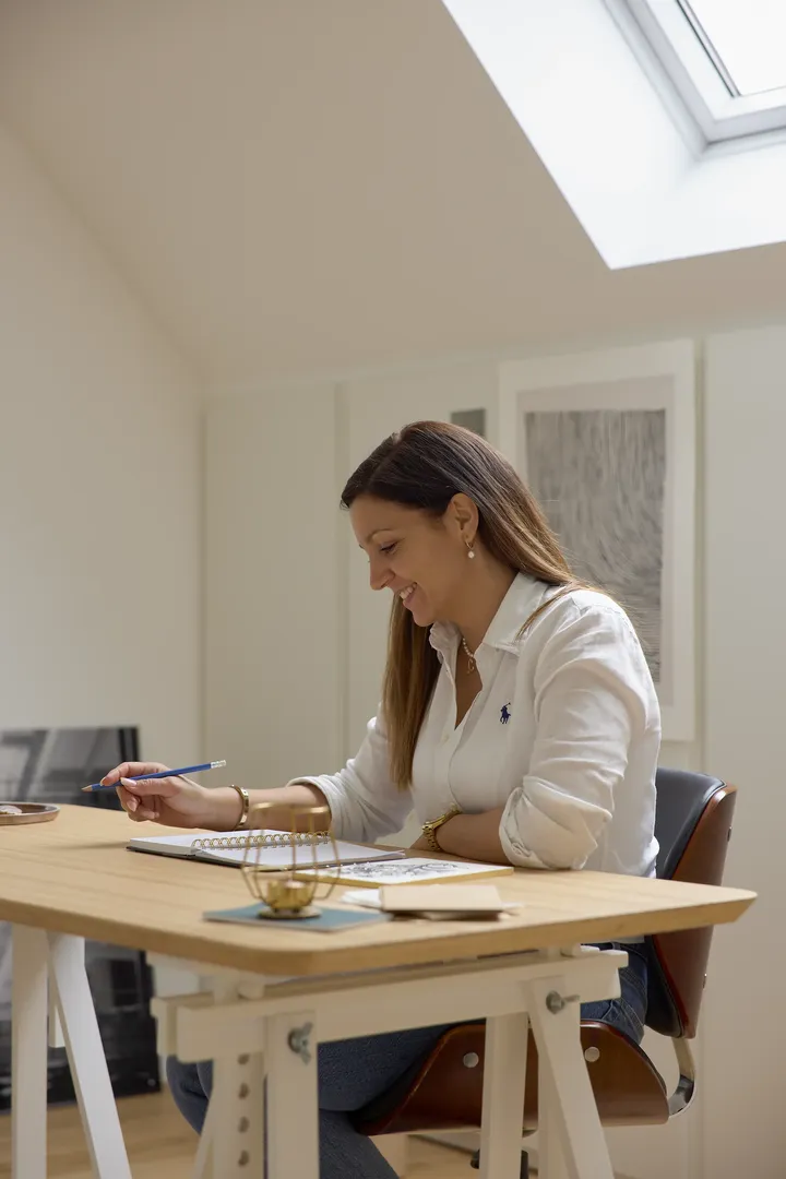 Žena radi za stolom ispod krovnog prozora, s prirodnim svjetlom koje osvjetljava radni prostor. | VELUX