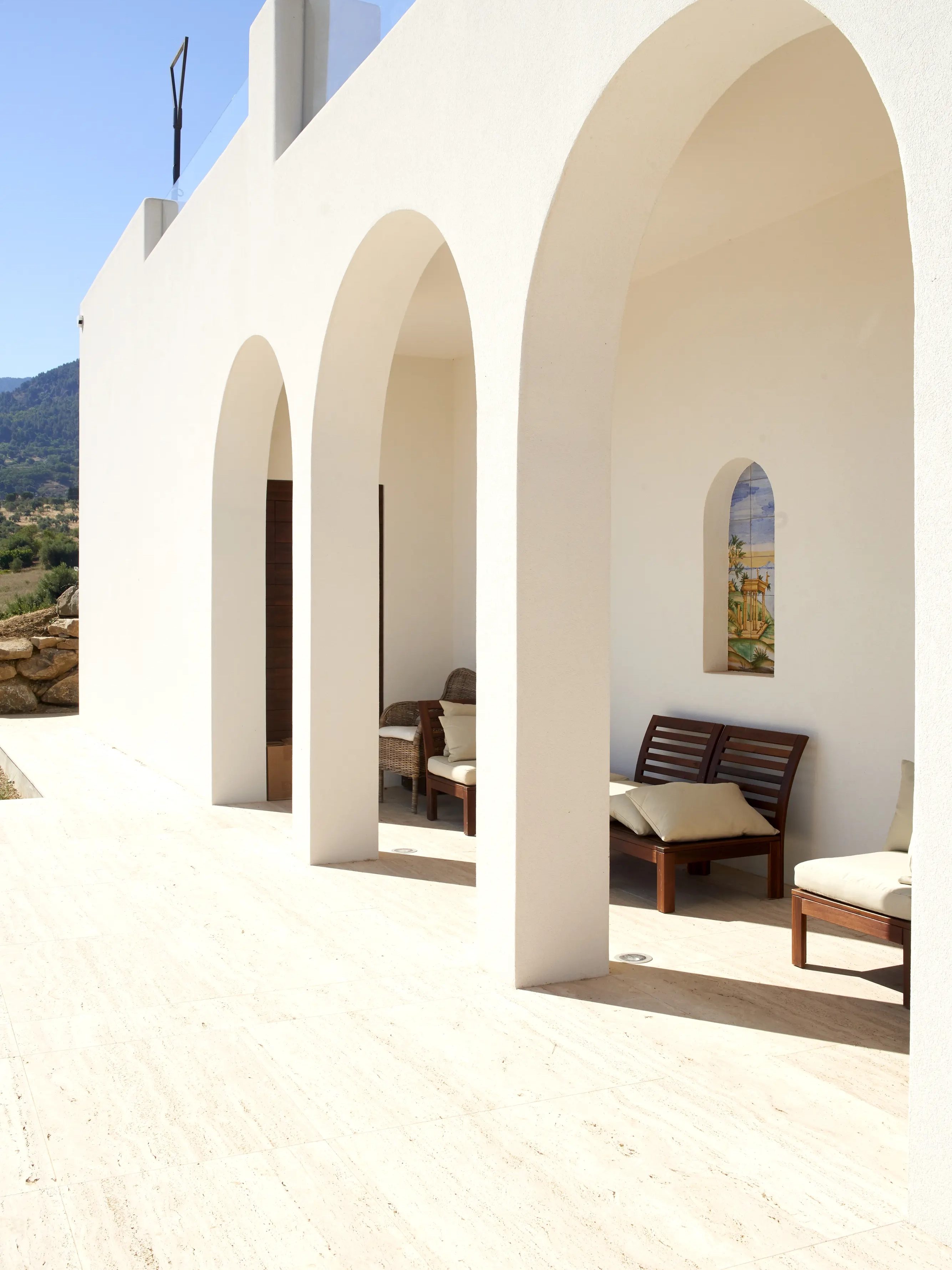Portico esterno con archi e pareti bianche, poltrone da esterno con cuscini.