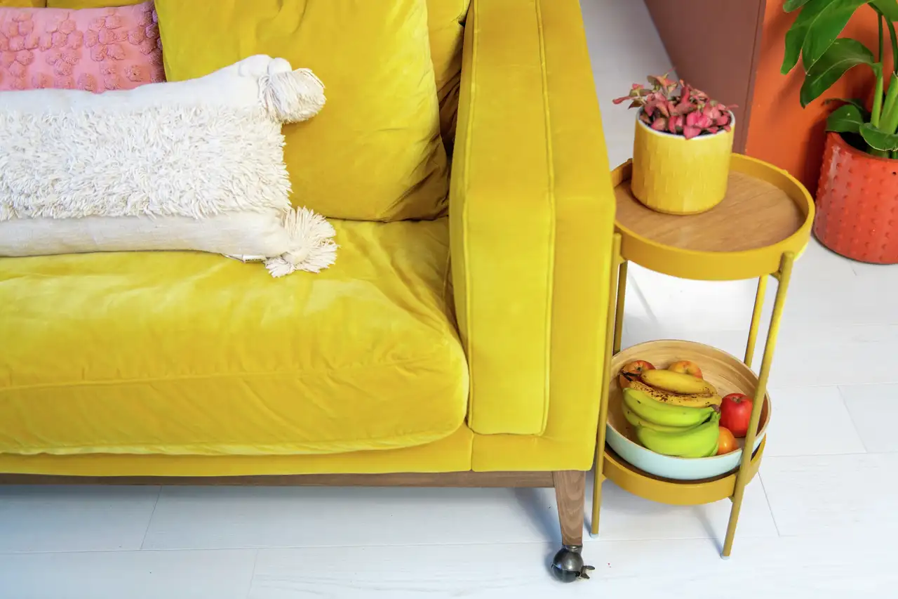 Canapé jaune en velours avec coussin clair, vase assorti et petit mobilier décoratif en tons vifs, dans une ambiance Dopamine decor