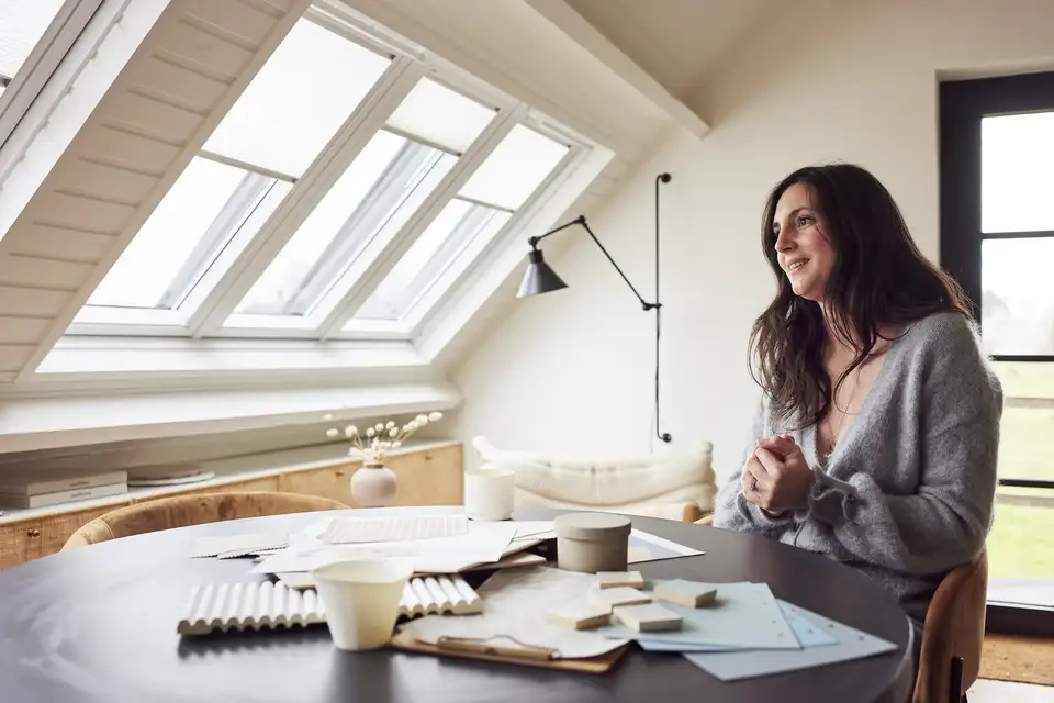 Een vrouw zit aan tafel en bestudeert de renovatieplannen voor haar woning. De VELUX dakvensters dragen bij aan een overvloed aan natuurlijk licht in de kamer.